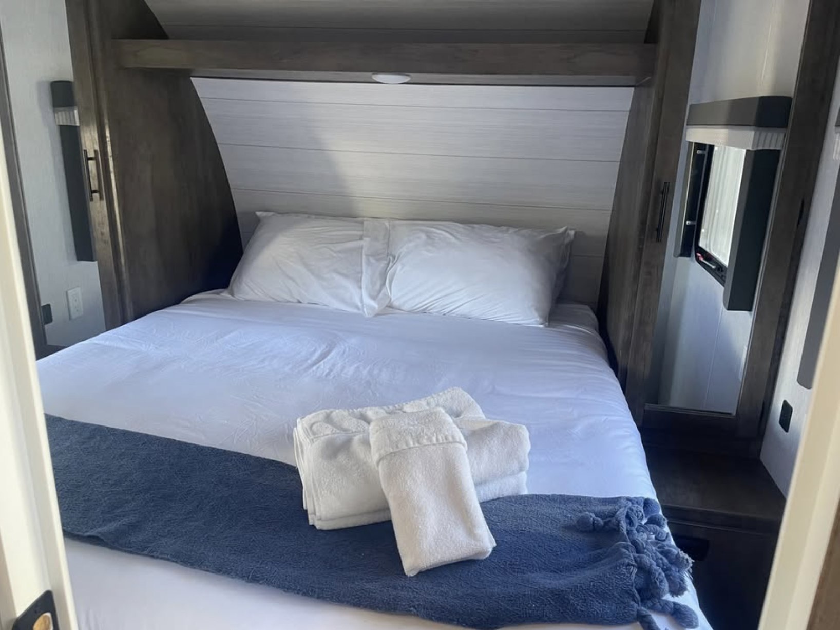 Cozy RV rental bedroom featuring a clean bed with white linens, pillows, a blue throw blanket, and neatly folded white towels.. Forest River Salem Cruise Lite 2022