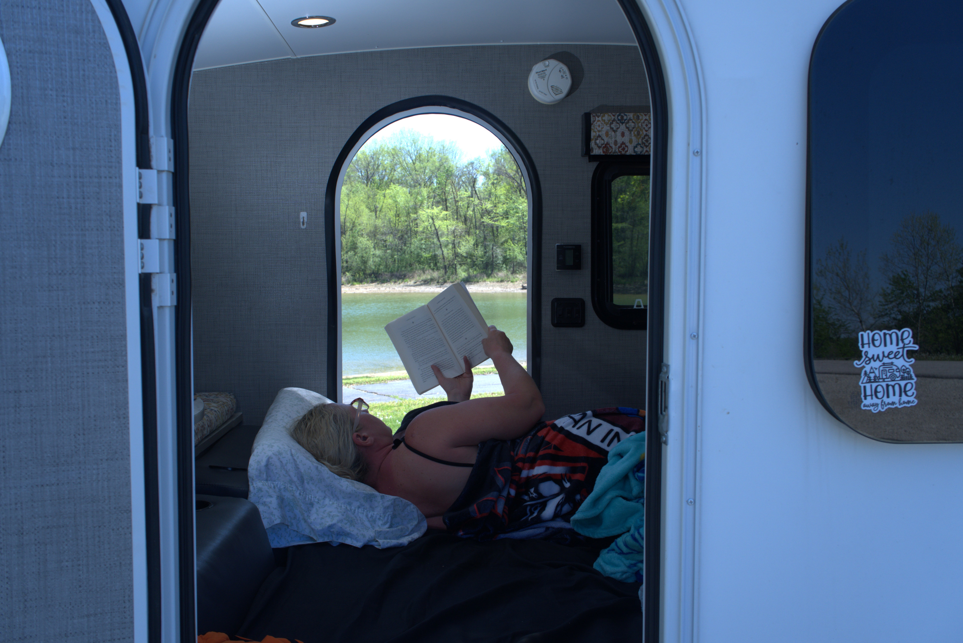 Woman relaxing in an RV rental, reading a book while enjoying a beautiful lake and forest view from inside.. InTech RV InTech RV Trailer 2018