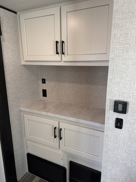 Modern RV rental interior: white overhead and base cabinets, light countertop, power outlets, and climate controls on textured walls.. Jayco Jay Flight 331BTS 2024