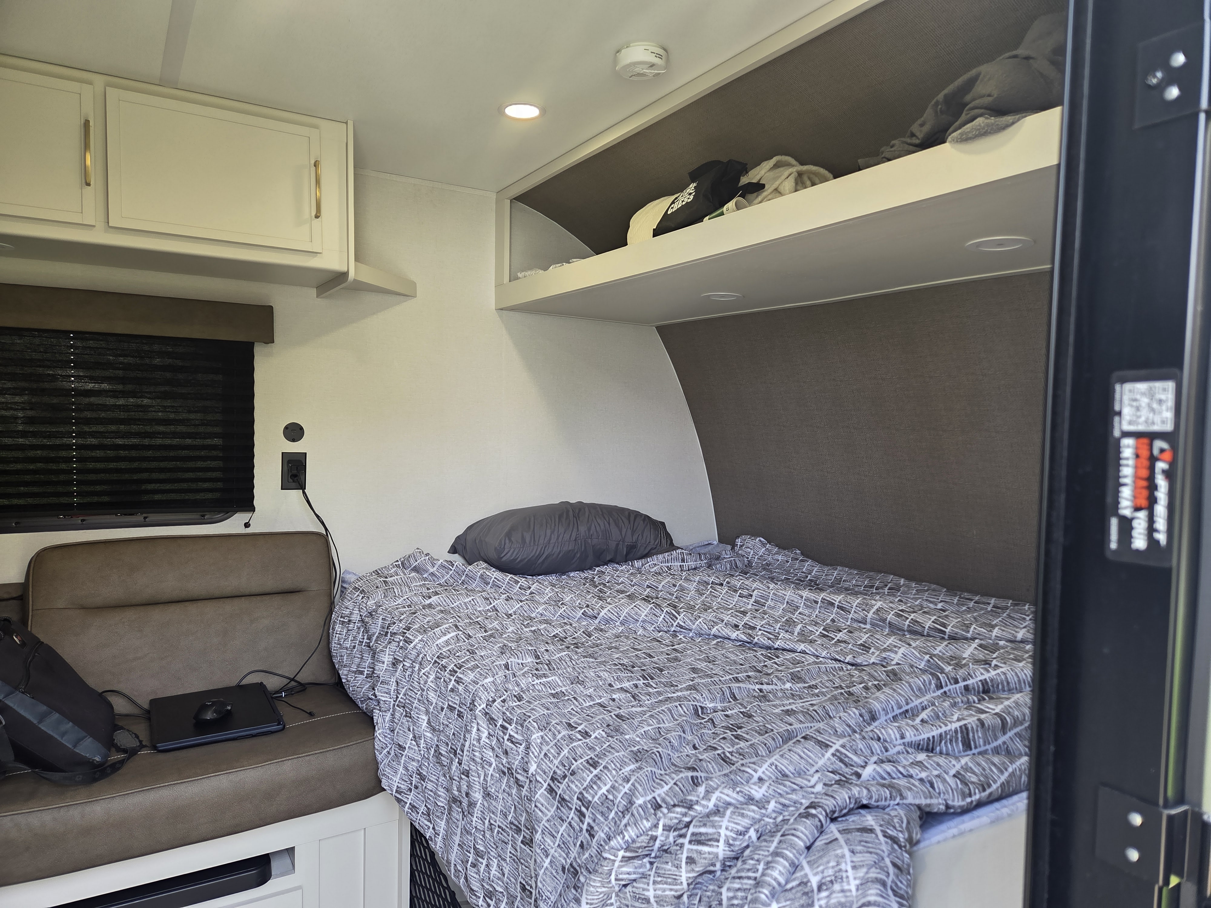 Cozy RV rental interior featuring a patterned bed, compact seating area, and practical overhead storage.. Grand Design Transcend One 2026