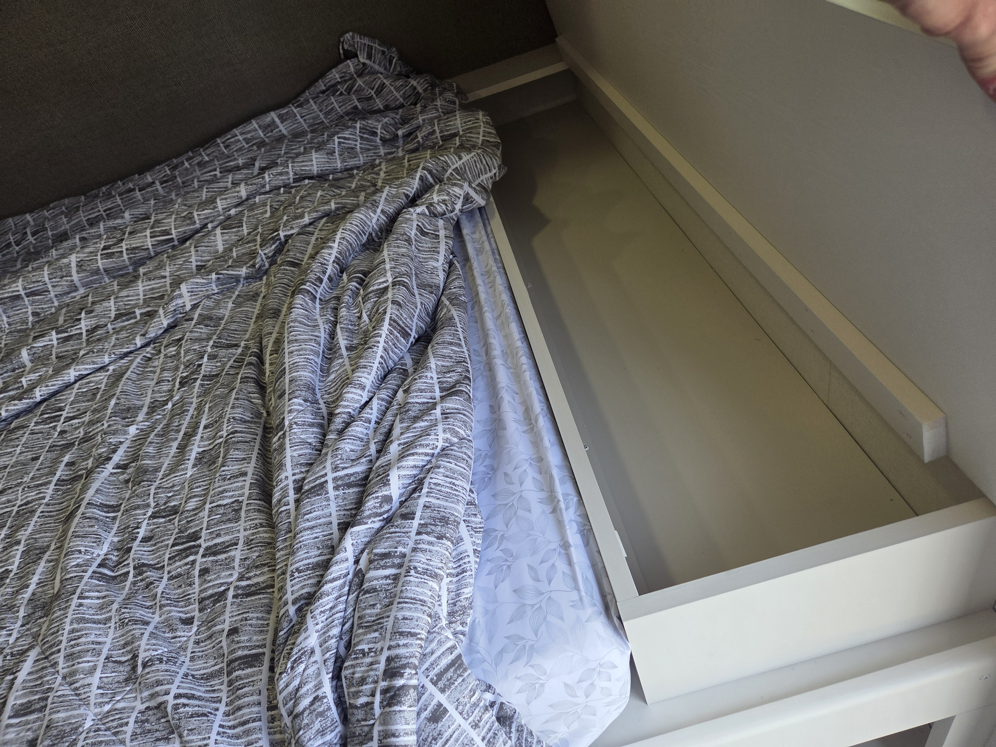 Cozy RV rental bed with patterned duvet and leaf-print sheet, revealing under-bed storage. Ideal for compact living.. Grand Design Transcend One 2026