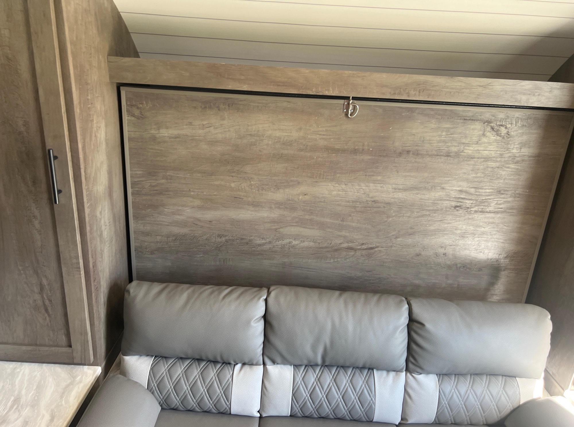 RV rental interior: Gray sofa against a wood-paneled wall, likely a foldable bed, with an adjacent cabinet.. Forest River Wildwood X-Lite 2021