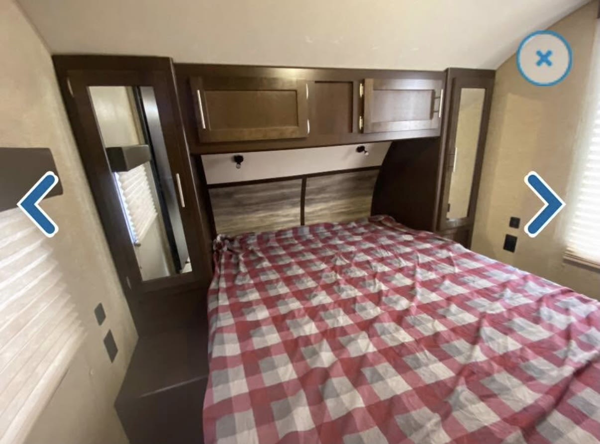 Cozy RV rental bedroom with a red and white checkered bed, overhead cabinets, and mirrored side wardrobes for your comfort.. Forest River Cherokee 2018