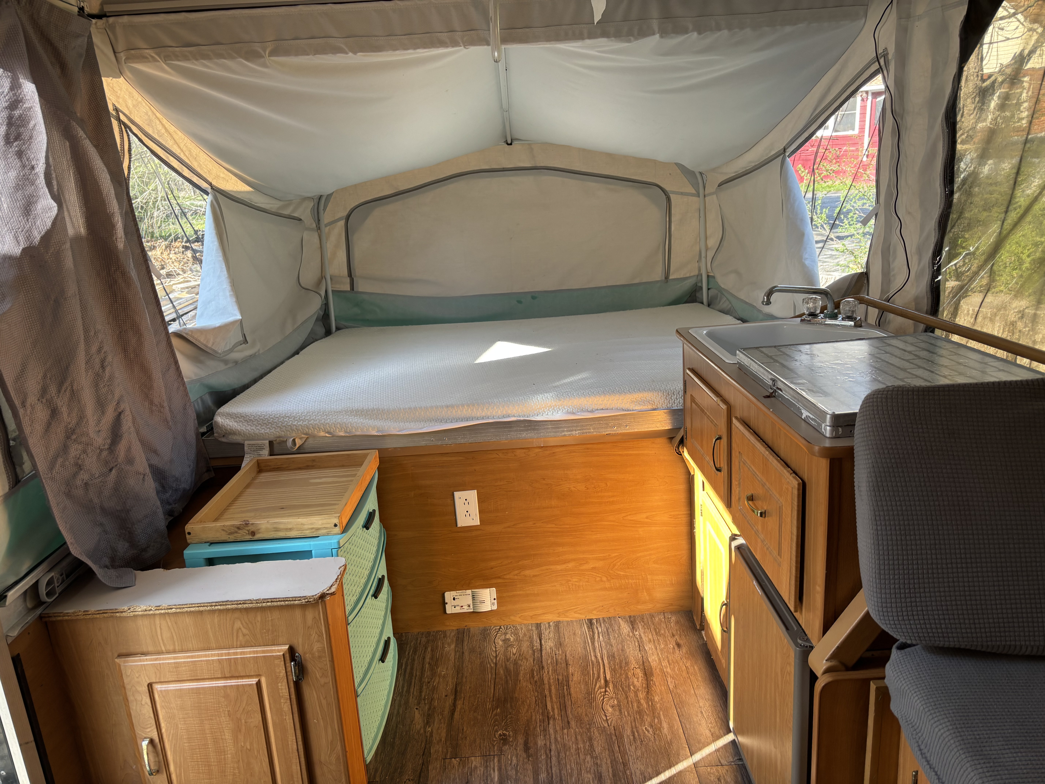 Bright pop-up camper rv rental interior with a bed, sink, and storage. Sunlight streams through the windows.. Coleman Grand Tour 2001