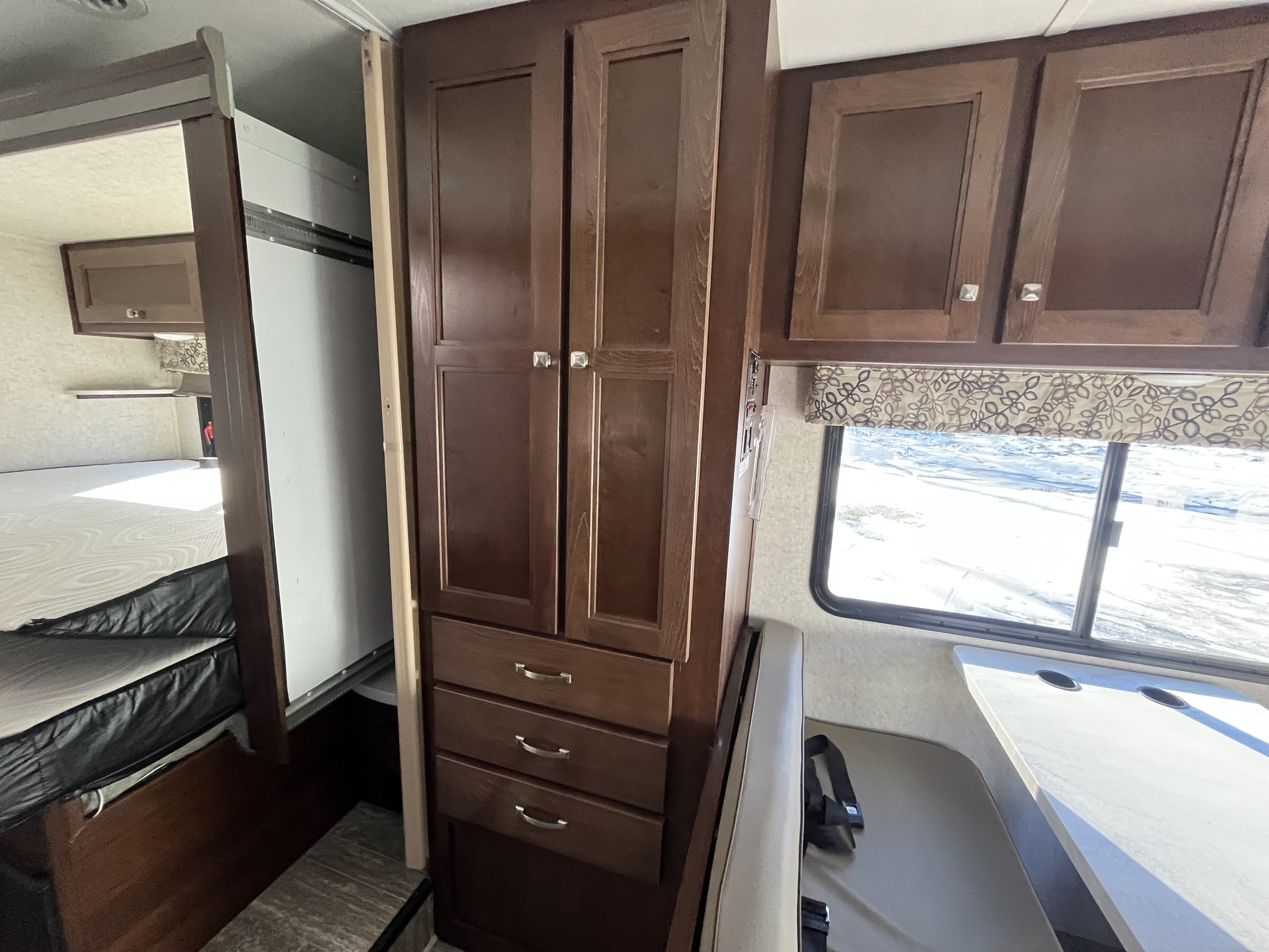 An RV rental's interior shows dark wood cabinets, a bed, and a dinette by a snowy window.. Forester Forester Motorhome 2020