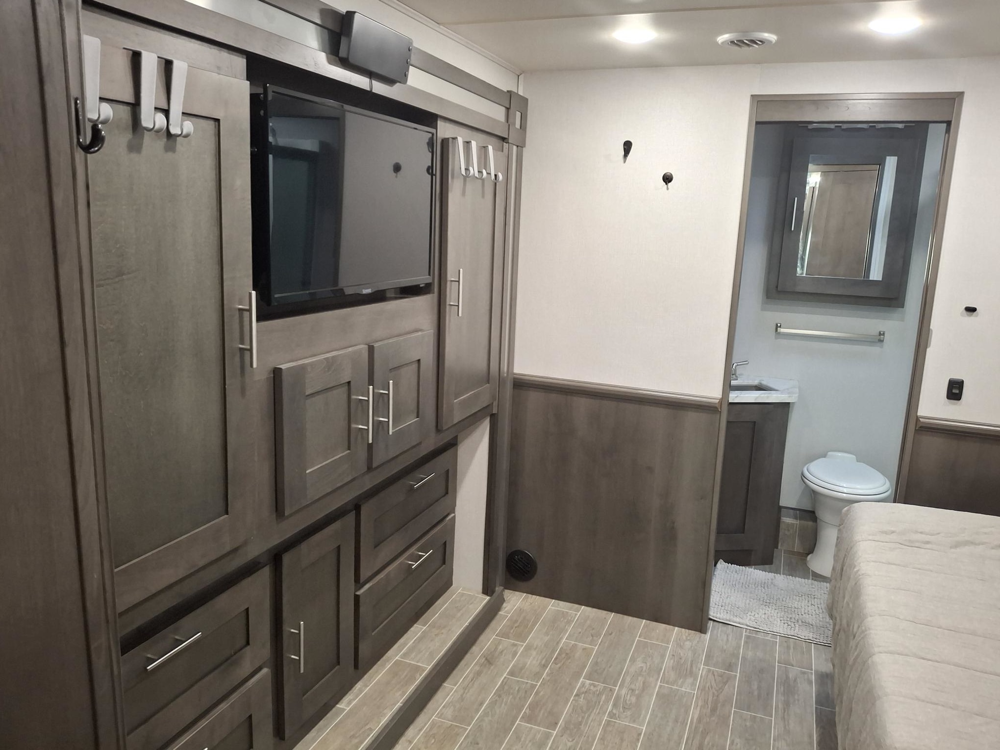 This rv rental bedroom features integrated storage, TV, and a partial bathroom view. Modern wood-look paneling and hooks visible.. Georgetown GT5 2021