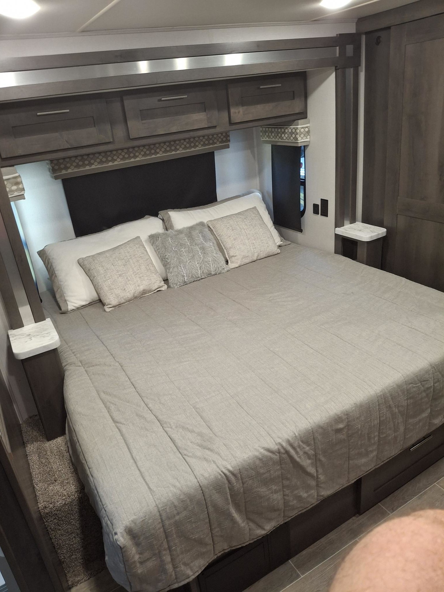 This rv rental features a cozy bedroom with a large bed, light gray bedding, dark overhead cabinets, and small bedside tables.. Georgetown GT5 2021