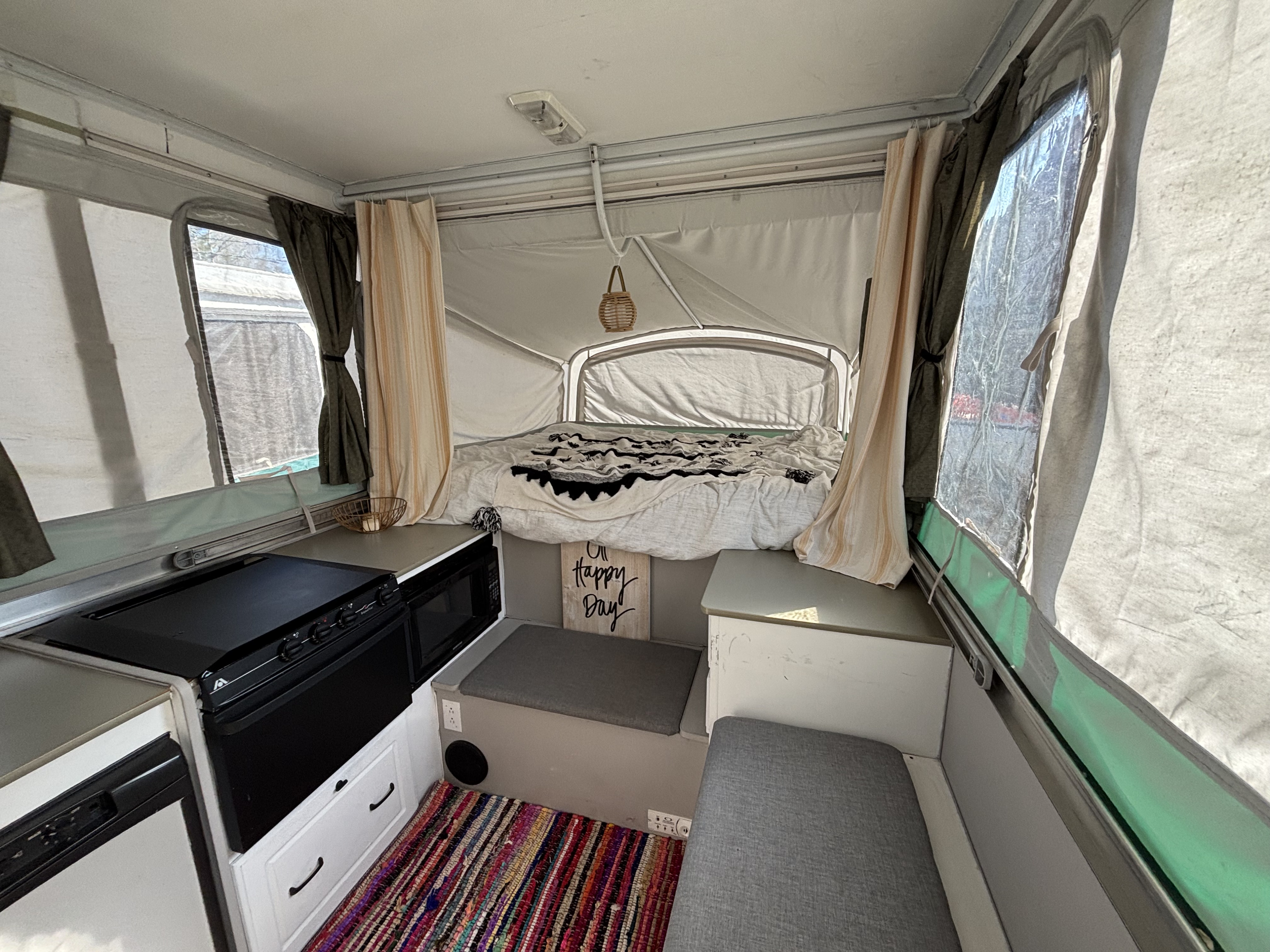 Cozy rv rental pop-up camper interior with bed, kitchen area, seating, and a colorful rug, perfect for a happy day.. Fleetwood Grand Tour 2004