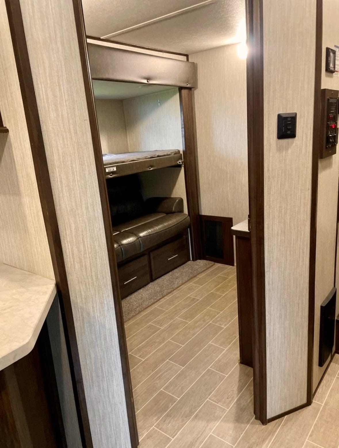 Modern RV rental interior featuring bunk beds, a brown sofa with storage, and stylish tiled flooring.. Forest River Cherokee Arctic Wolf 2020