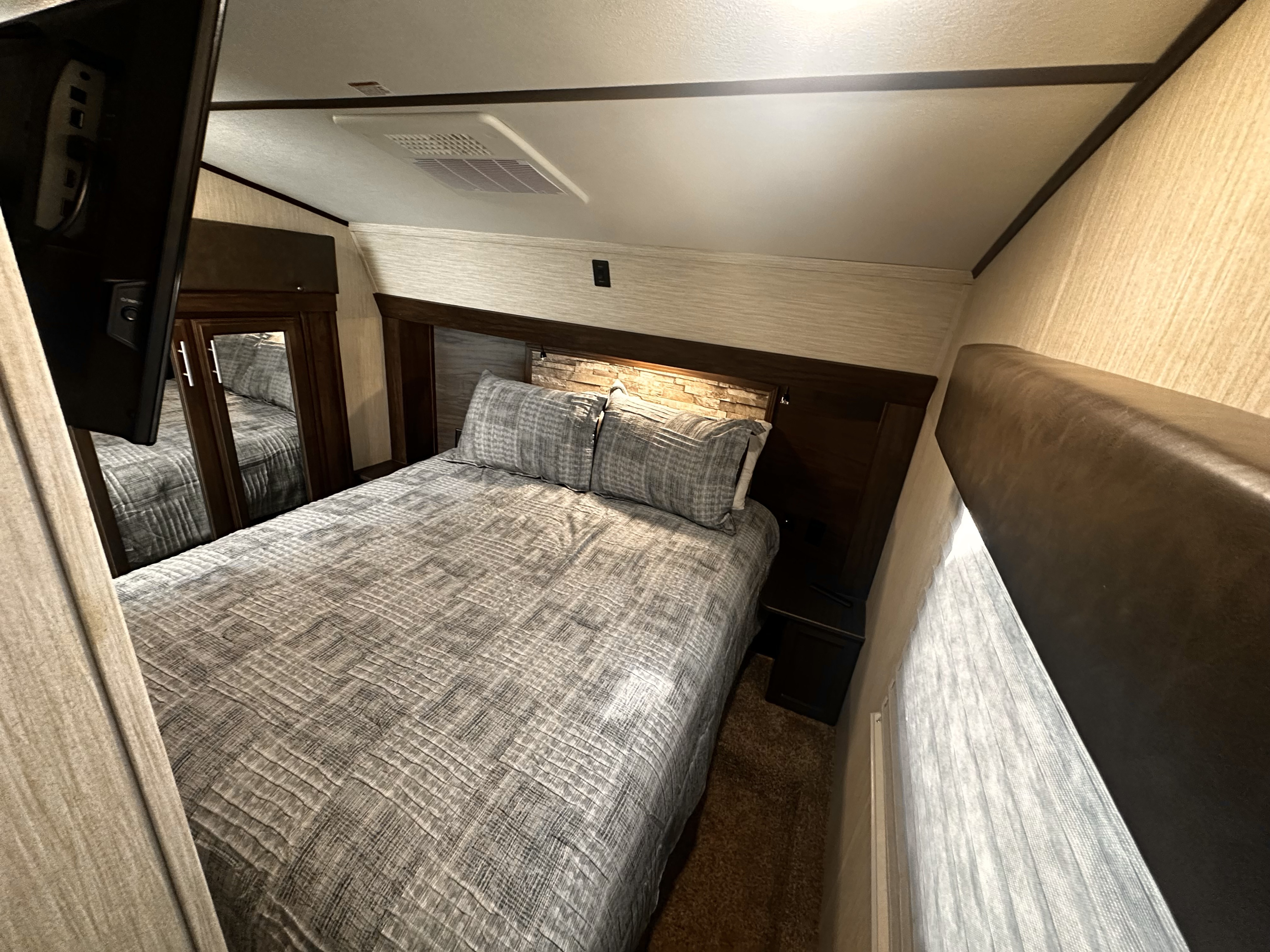 Cozy queen bedroom in an RV rental, featuring quilted bedding, storage, a TV, and AC unit for comfortable travels.. Forest River Cherokee Arctic Wolf 2020