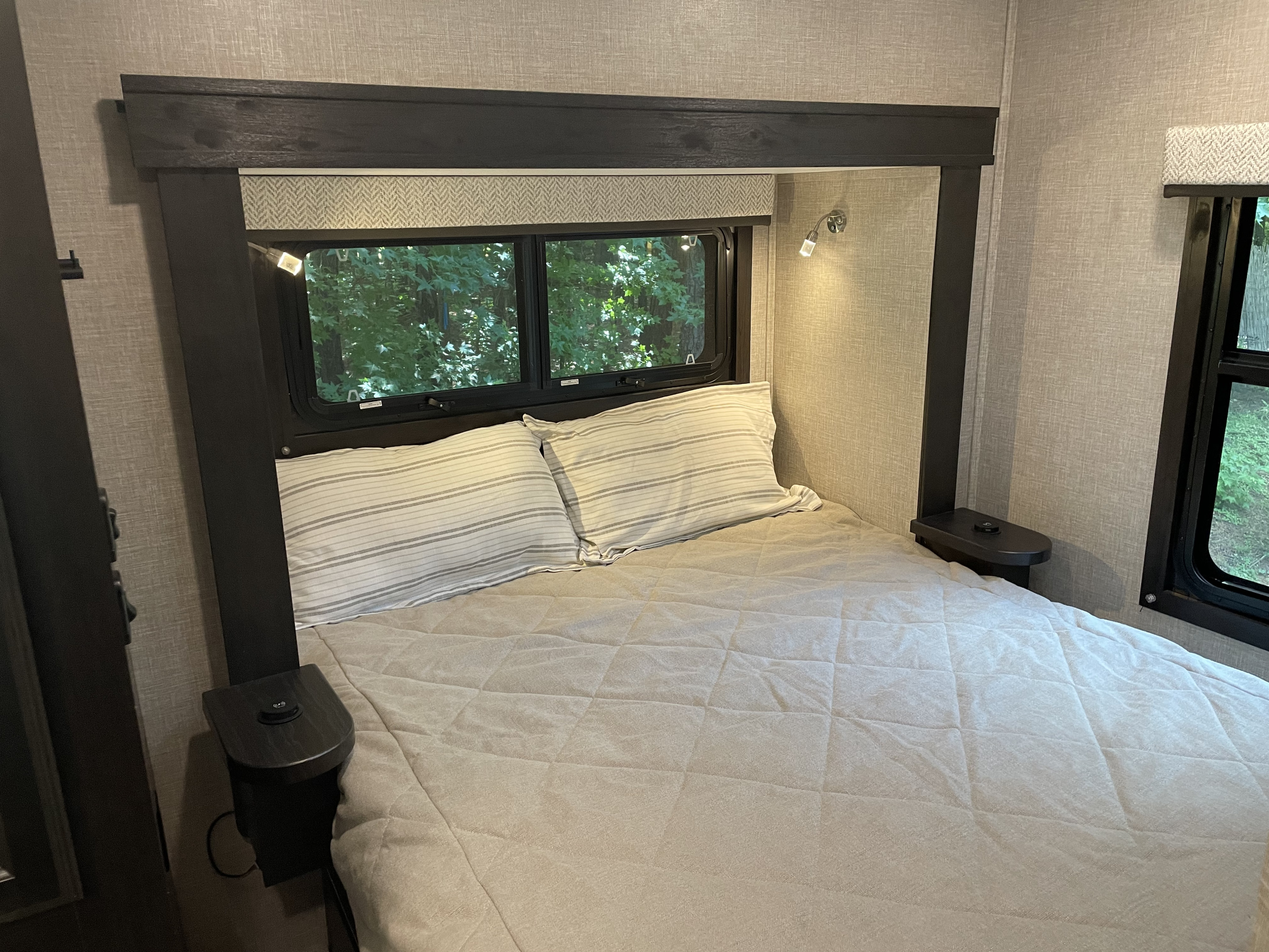 Cozy RV rental bedroom with queen bed, green views, built-in nightstands with charging ports, and reading lights.. Jayco Redhawk SE 2023