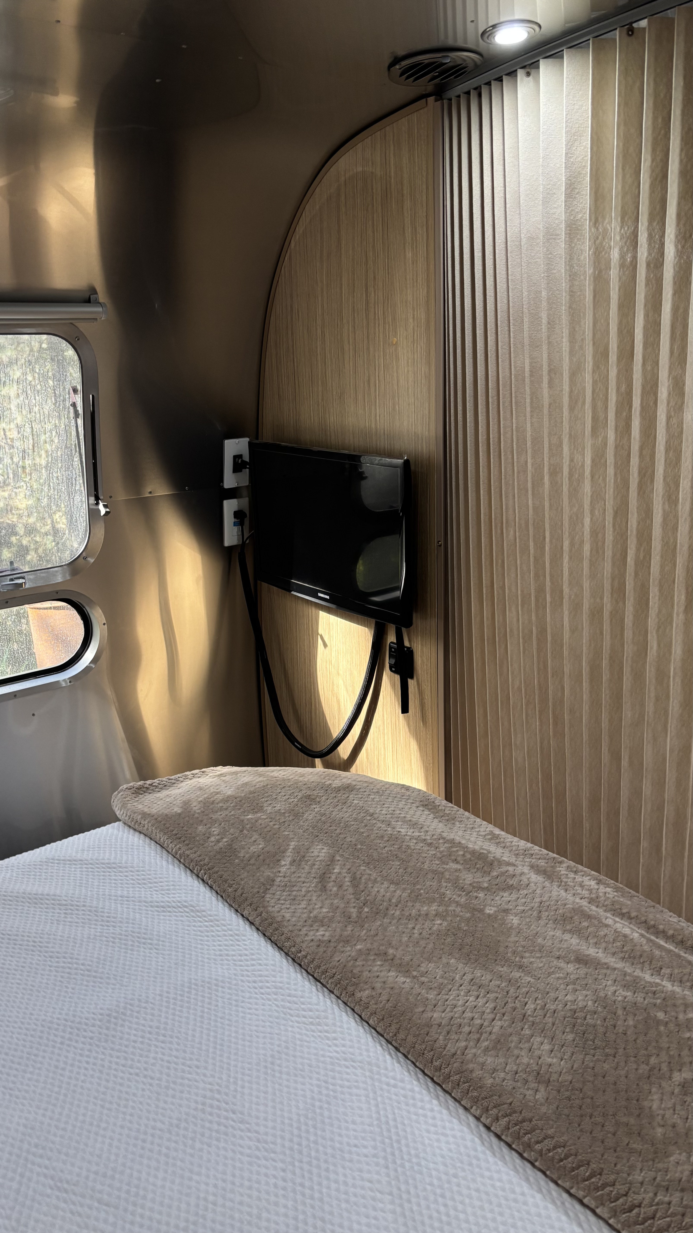 Cozy Airstream rv rental bedroom with a mounted TV, bed, and window. Ideal for a comfortable travel experience.. Airstream Flying Cloud 2018