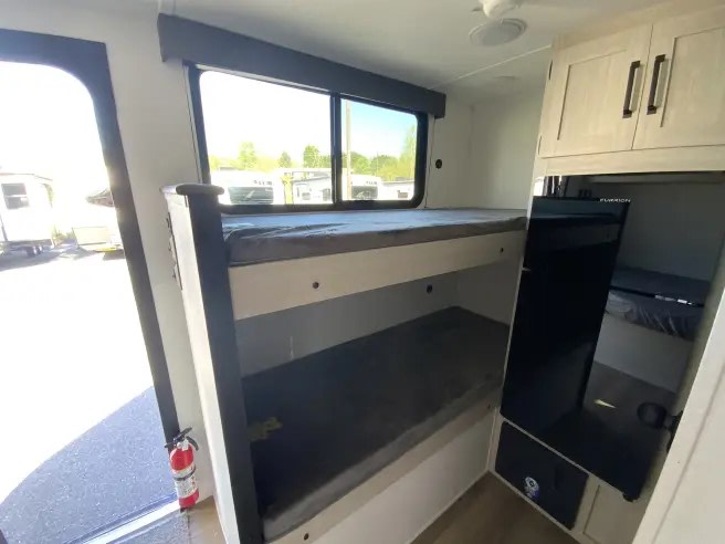 View inside an rv rental, featuring bunk beds, a compact kitchen with upper cabinets, and a door with a fire extinguisher.. Forest River Puma 2025