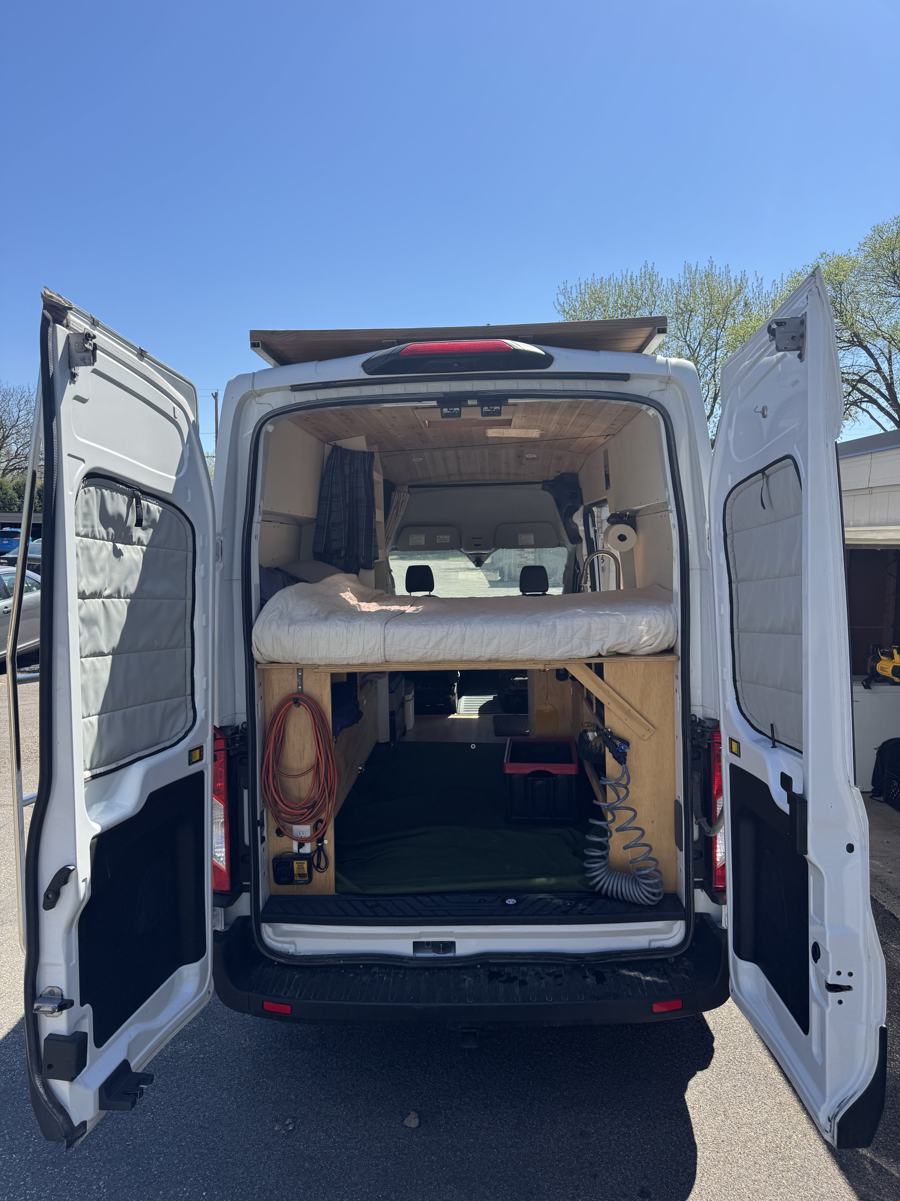 RV rental camper van with open back doors, showcasing a custom interior, elevated bed, storage, and utilities.. Ford Transit 250 AWD 2022