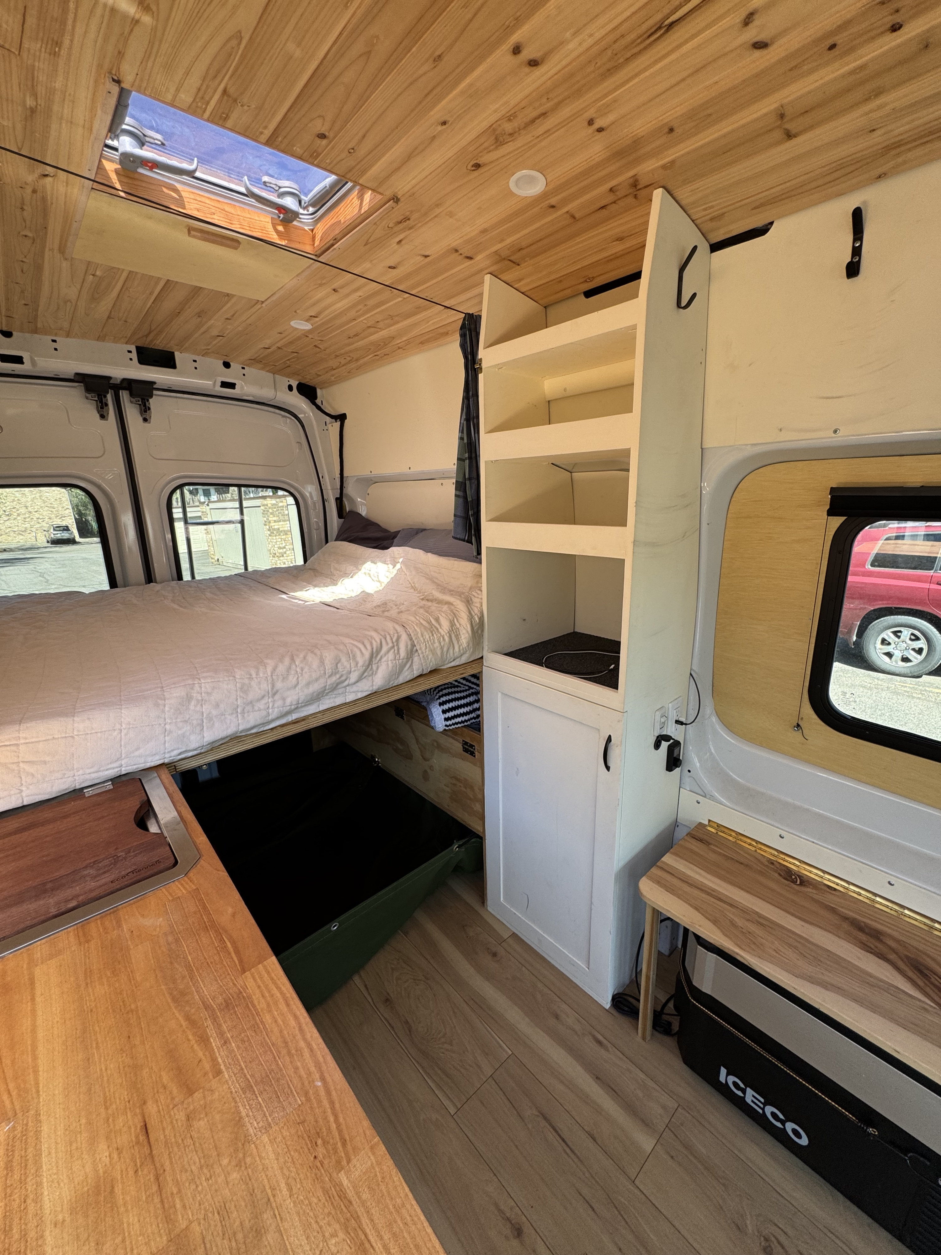 RV rental: Inside a van conversion with a bed, wood-paneled ceiling, compact kitchen counter, and white storage.. Ford Transit 250 AWD 2022