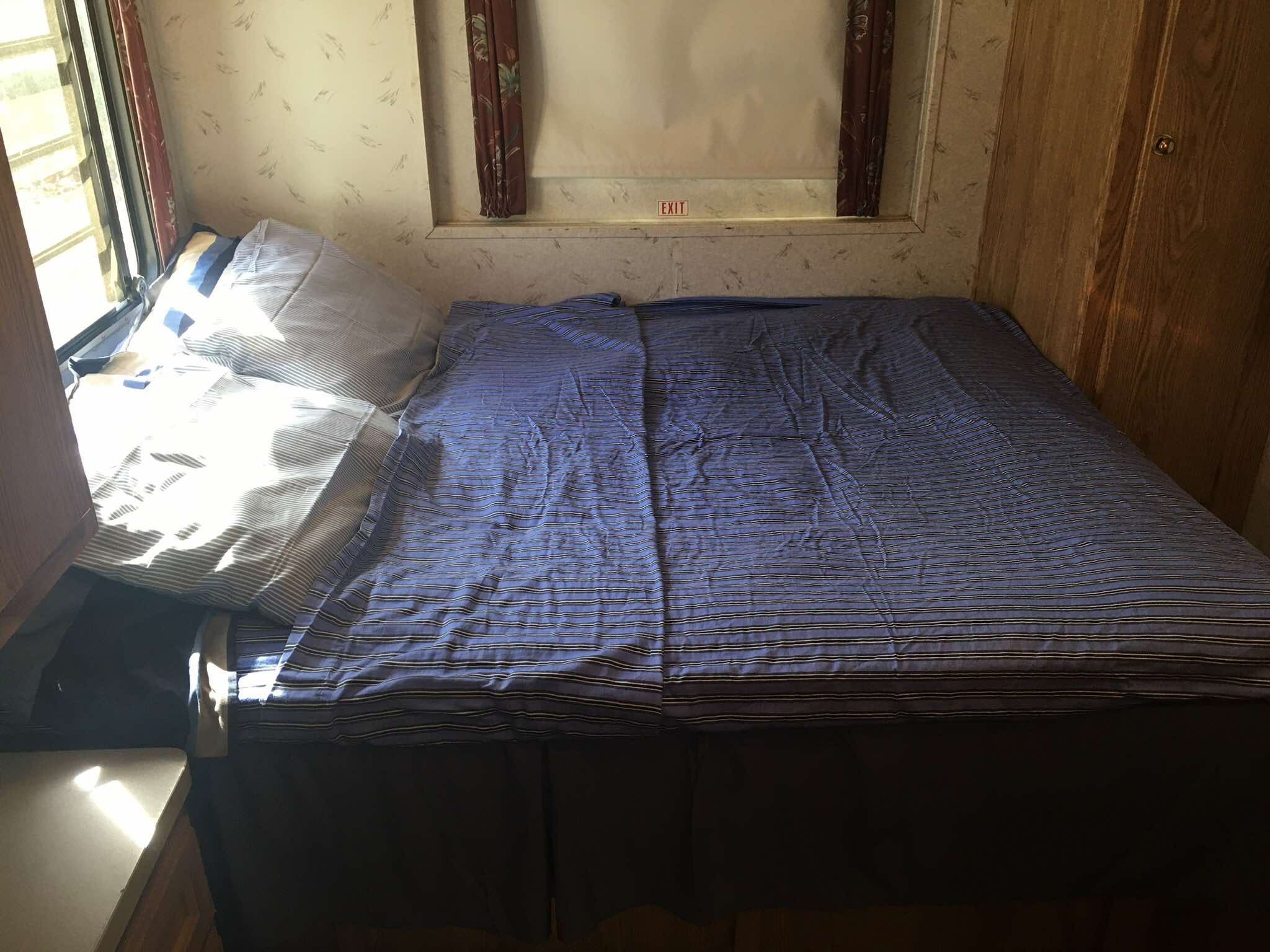 Inside an RV rental: a bedroom with a blue striped bed, pillows, window on the left, and an overhead EXIT sign.. Georgie Boy Pursuit 1995