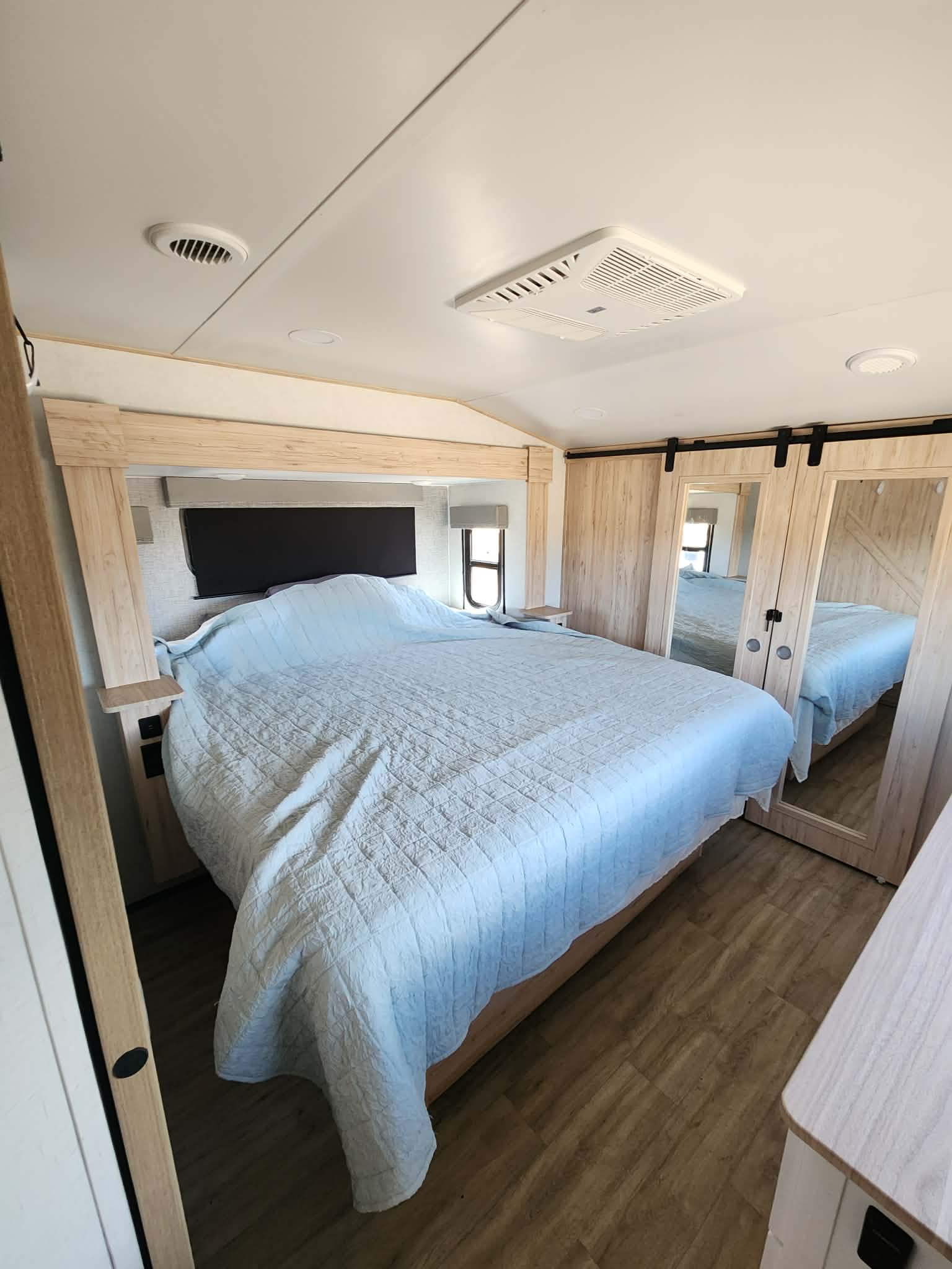 Modern RV rental bedroom featuring a large bed, light wood headboard, and mirrored sliding closet doors.. Alliance RV Avenue 2022