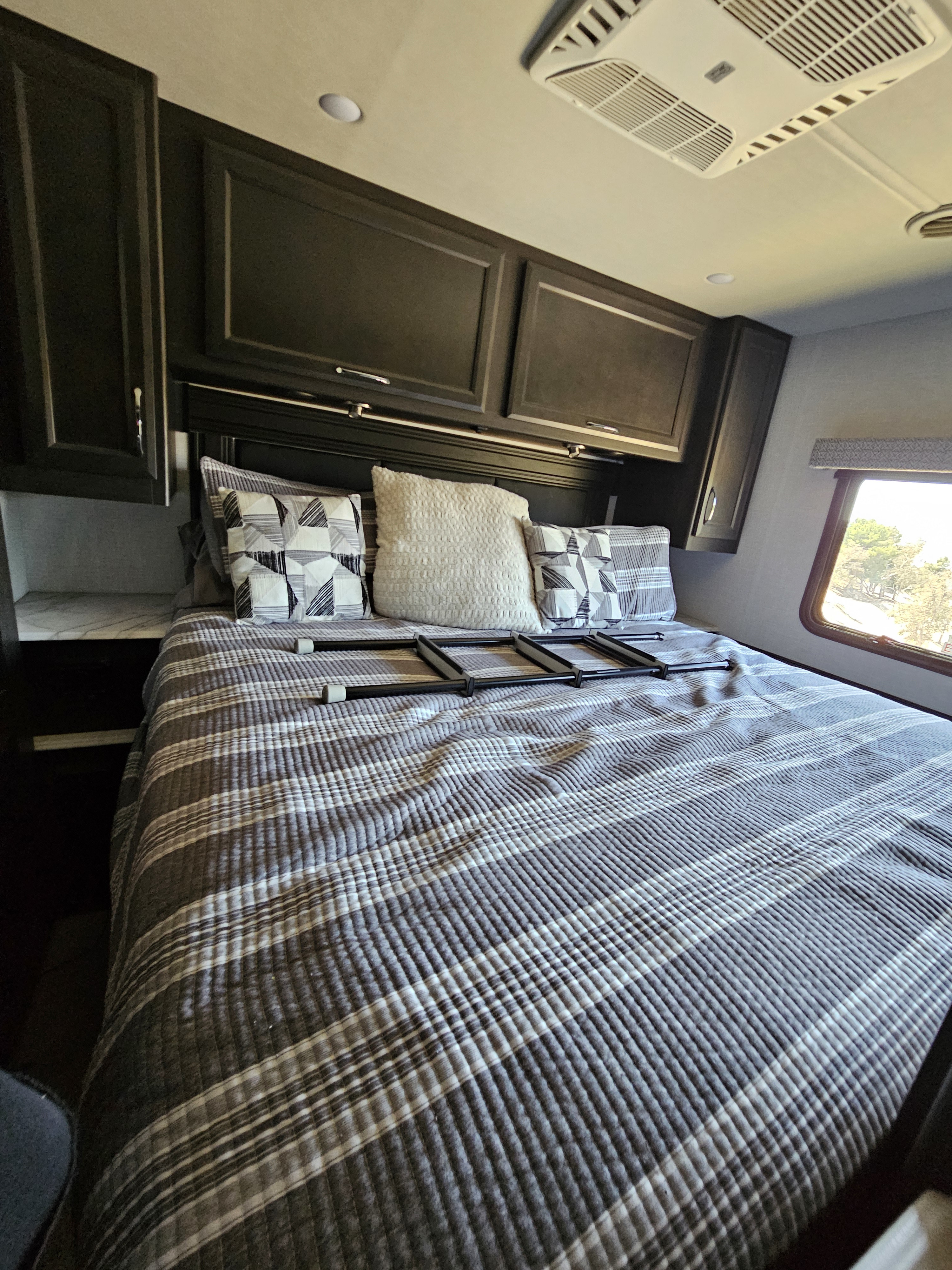 RV rental bedroom: a comfy striped bed with a ladder, overhead cabinets, and a scenic window view.. Fleetwood Flex 2024