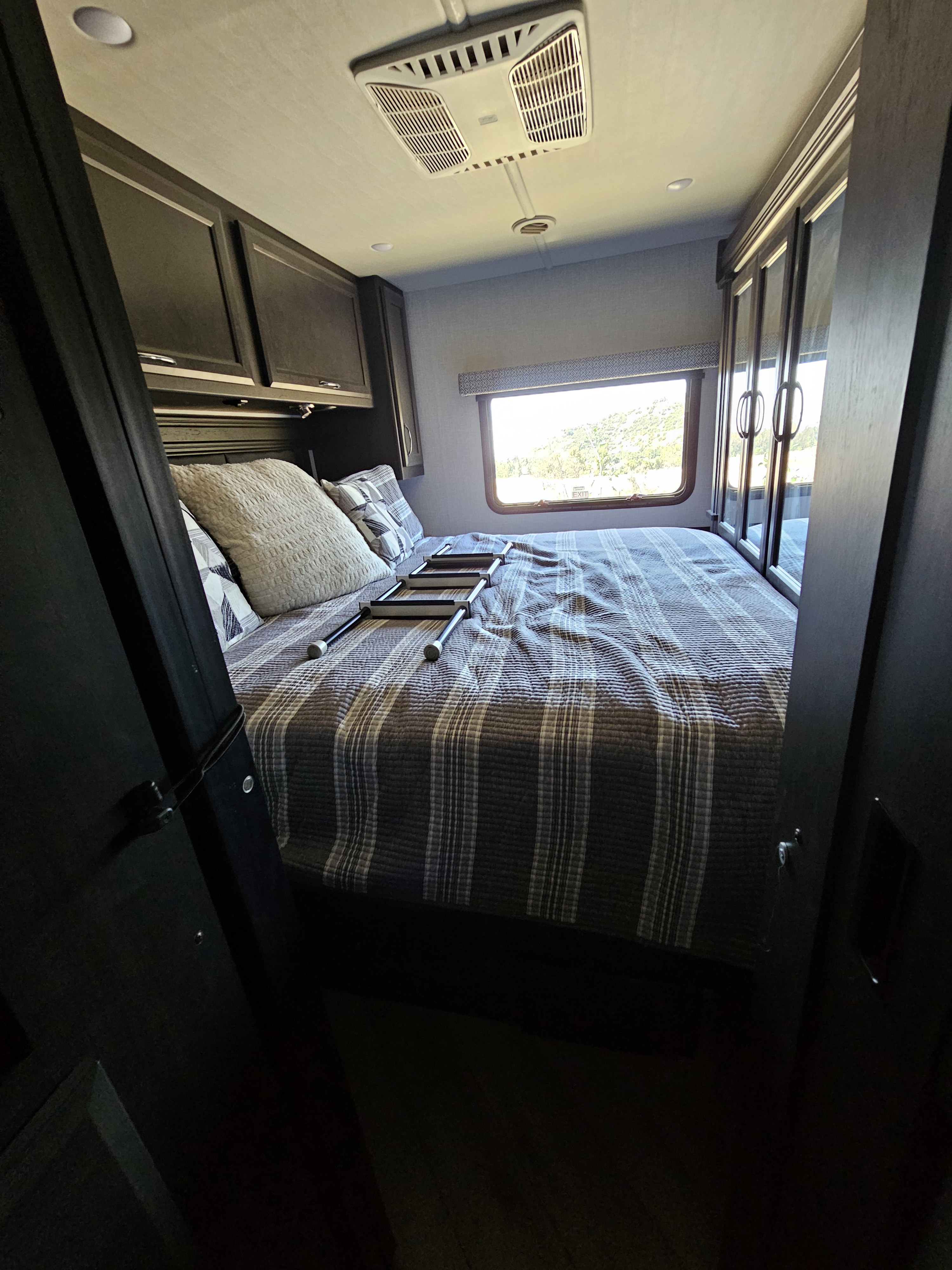 Cozy rv rental bedroom with striped bedding, overhead cabinets, and a scenic window view, perfect for comfortable travel.. Fleetwood Flex 2024
