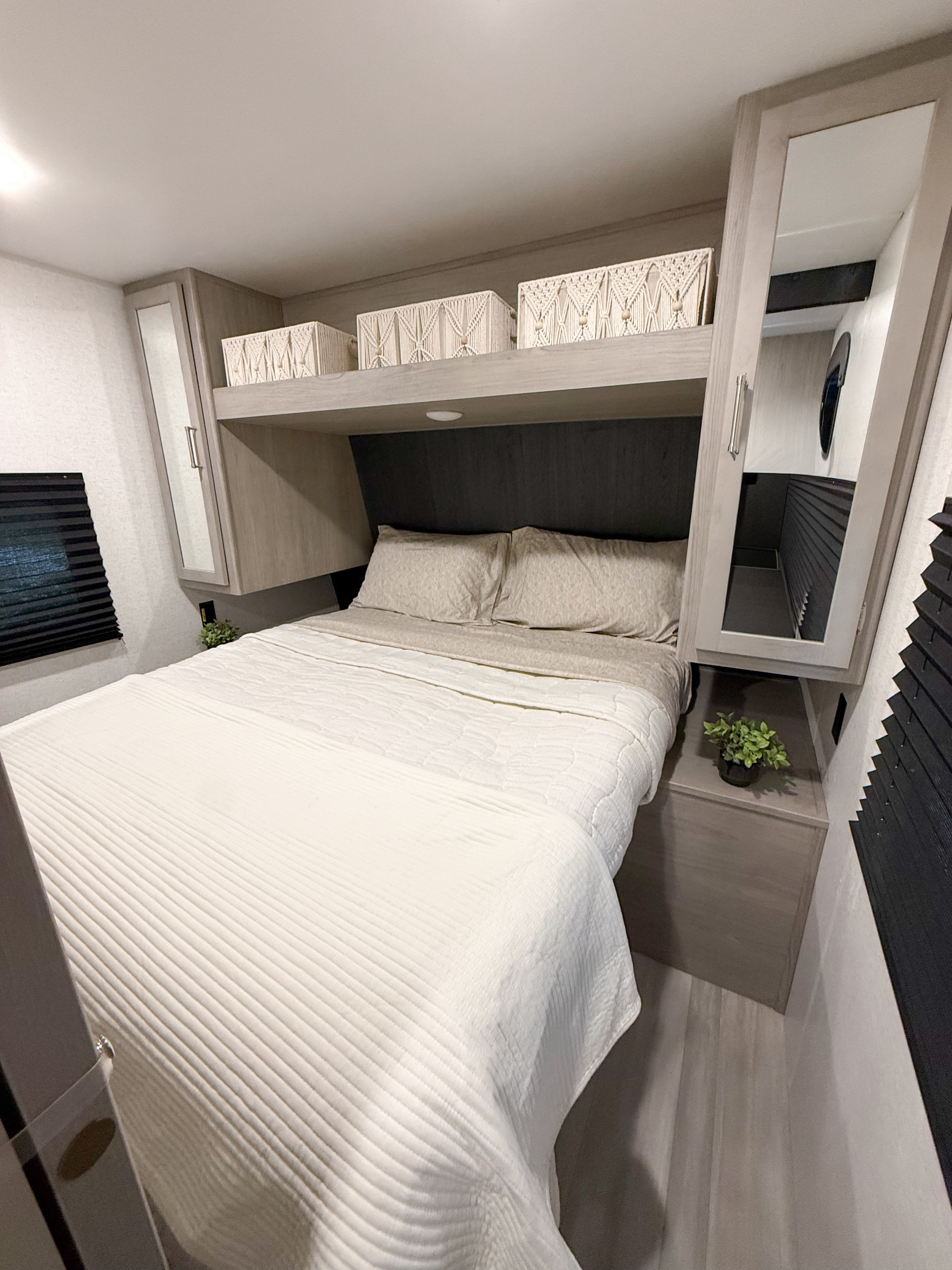 This modern RV rental bedroom features a comfy bed, light wood cabinetry, macrame storage baskets, and mirrored wardrobes. A cozy retreat.. Keystone RV Springdale 25th Anniversary 2024