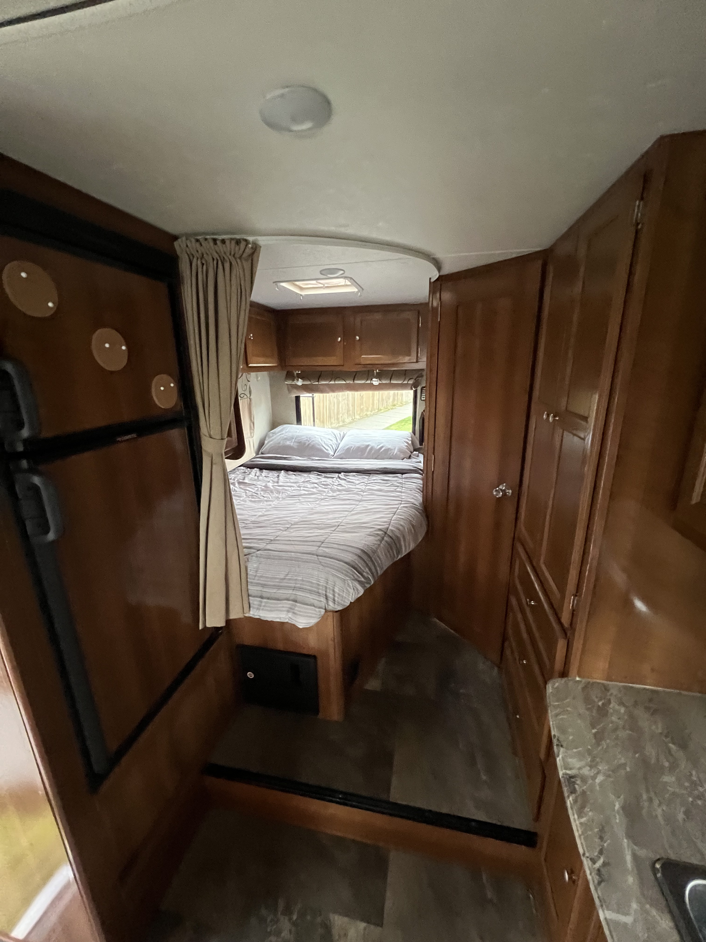 This RV rental interior features a cozy, compact bedroom with a bed, overhead wooden cabinets, a refrigerator, and a small counter.. coachmen 230cb 2019