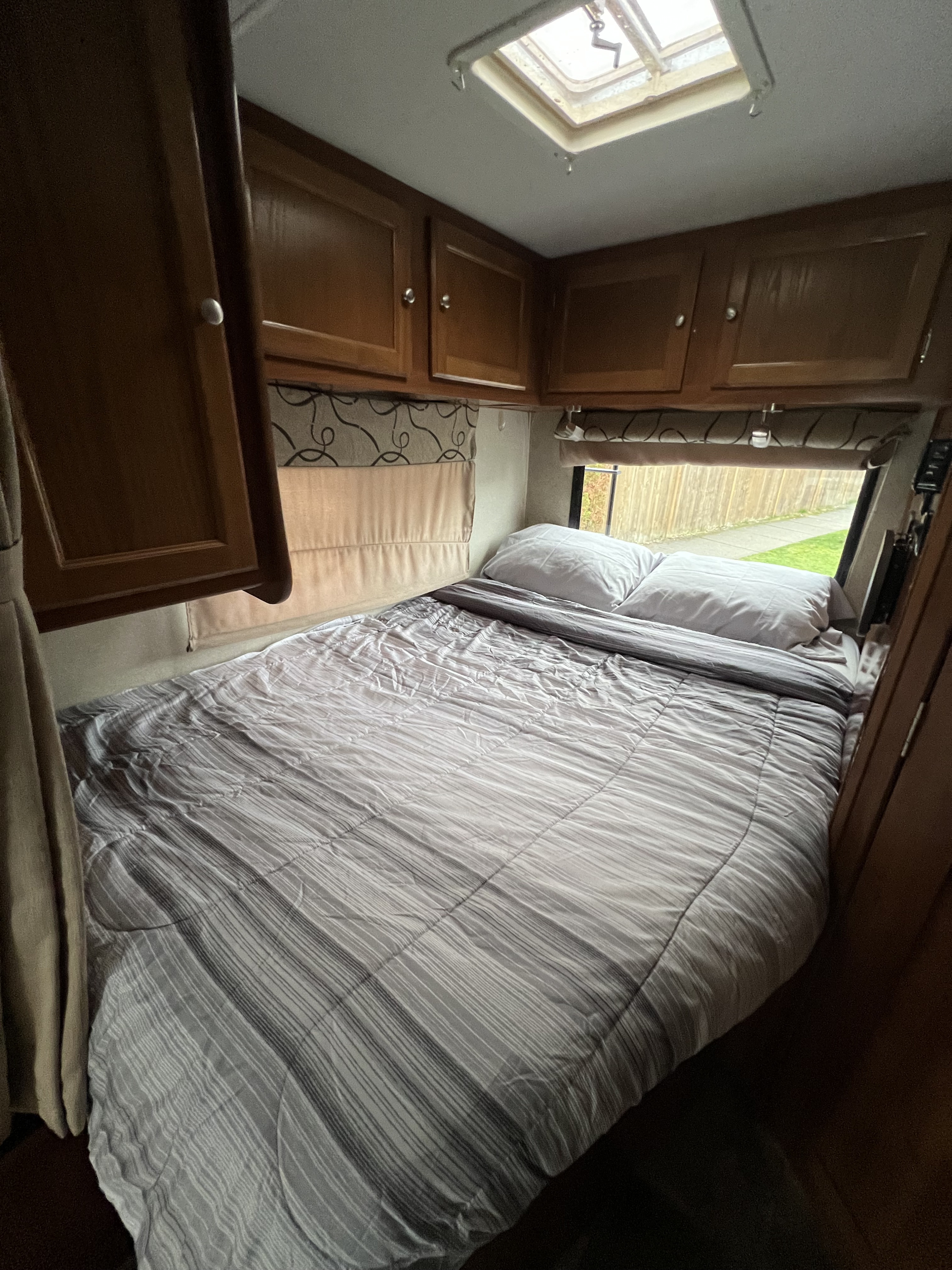 Cozy RV rental bedroom with a striped bed, pillows, wood cabinets, and skylight. Great for travel!. coachmen 230cb 2019