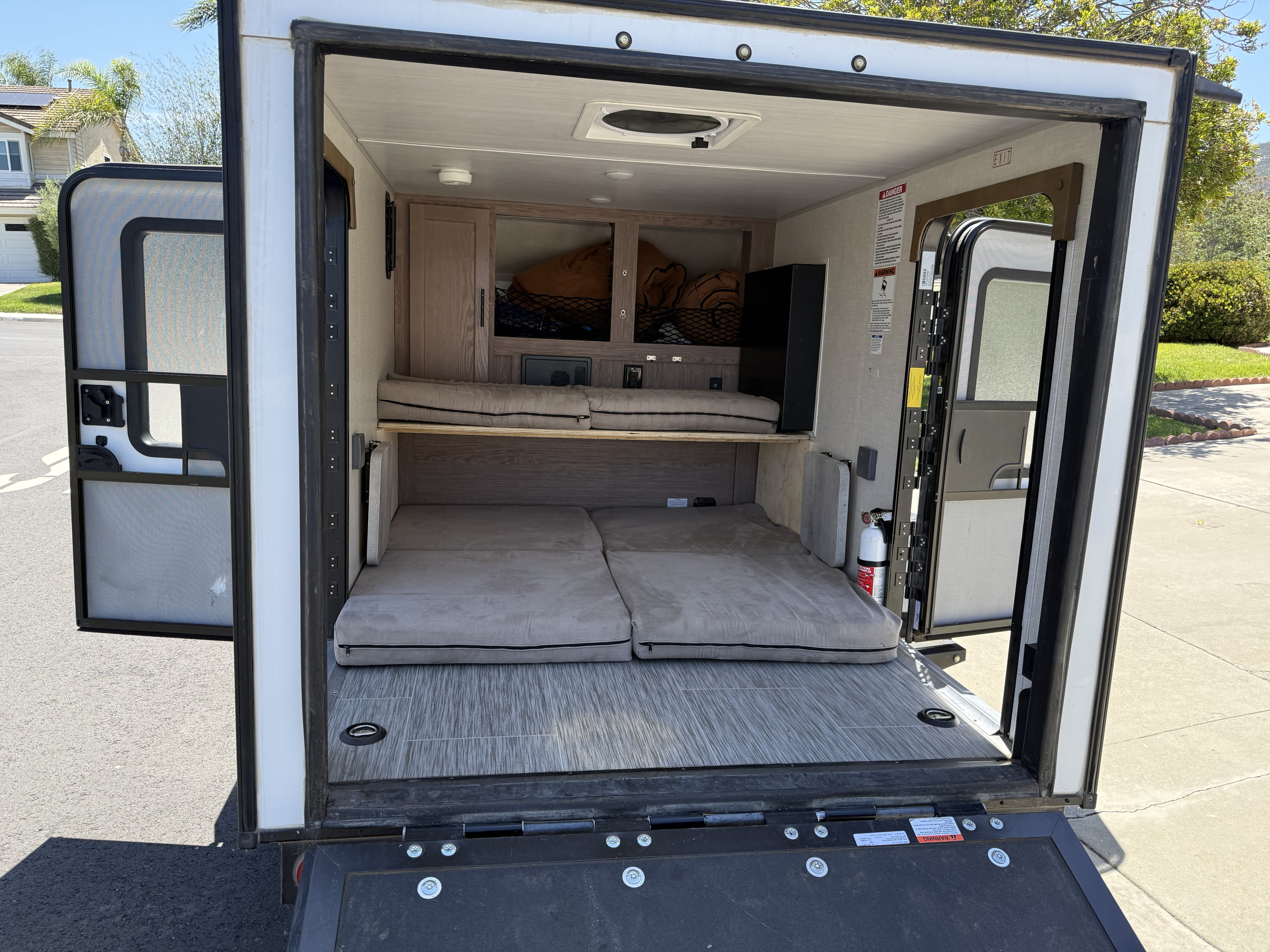 RV rental interior from open rear ramp: showing dual cushioned sleeping areas, overhead storage, and a fire extinguisher.. No Boundaries 10 Toy Hauler 2022