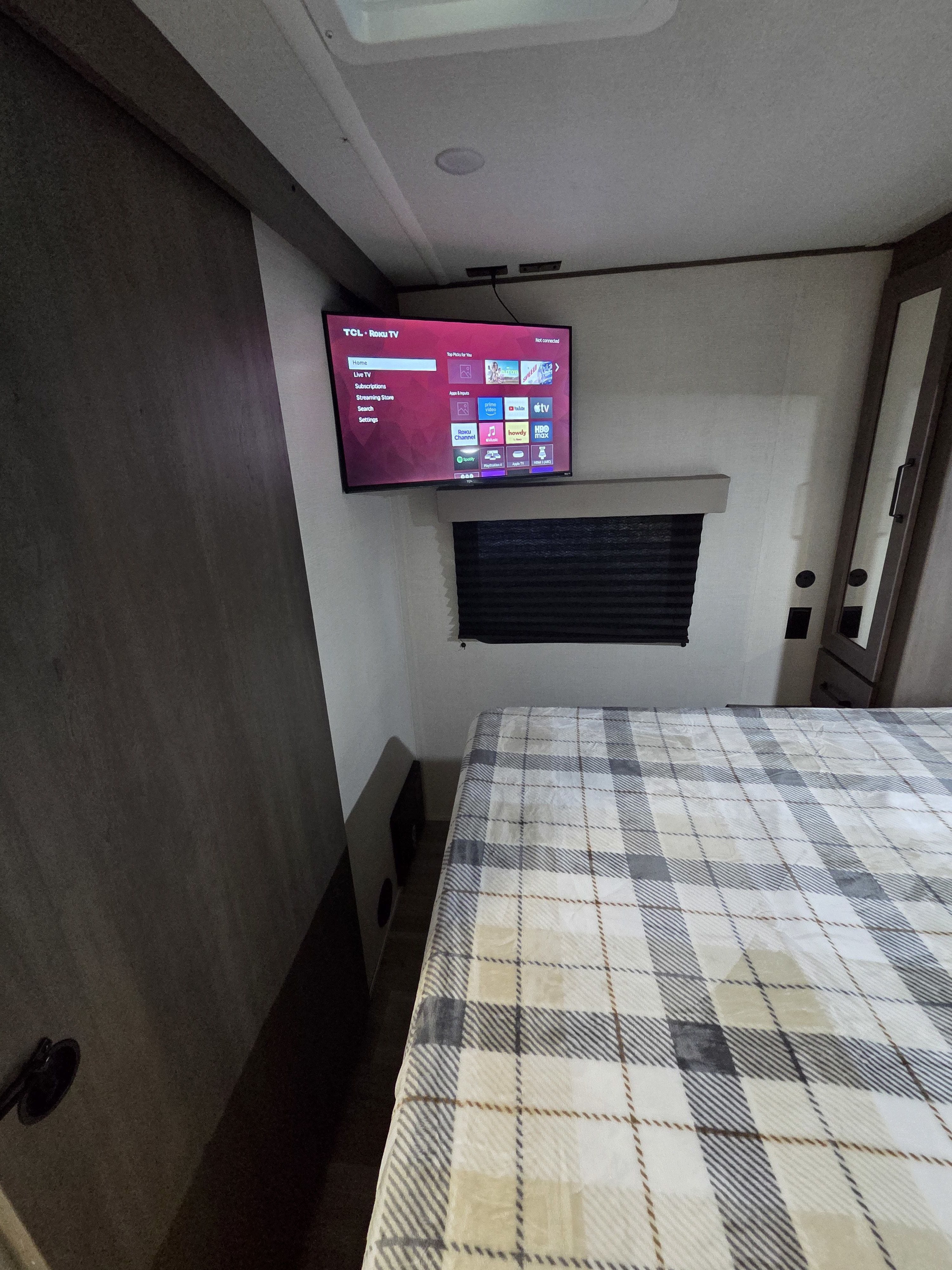 Cozy RV rental bedroom featuring a mounted TCL Roku TV, a bed with a plaid blanket, and compact design.. Grand Design Transcend Xplor 2024