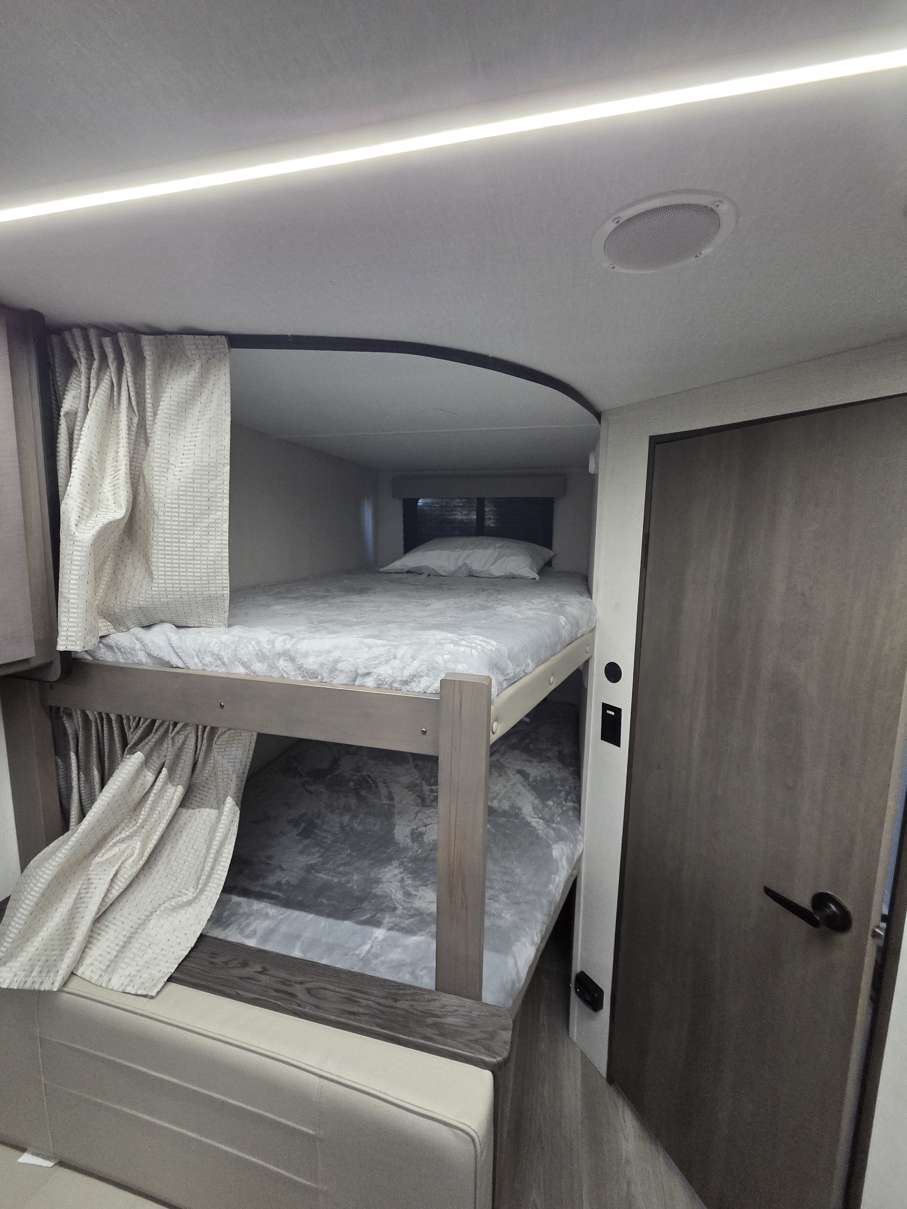 This RV rental features cozy bunk beds with curtains for privacy, a ceiling light, and speaker, ideal for compact sleeping.. Grand Design Transcend Xplor 2024
