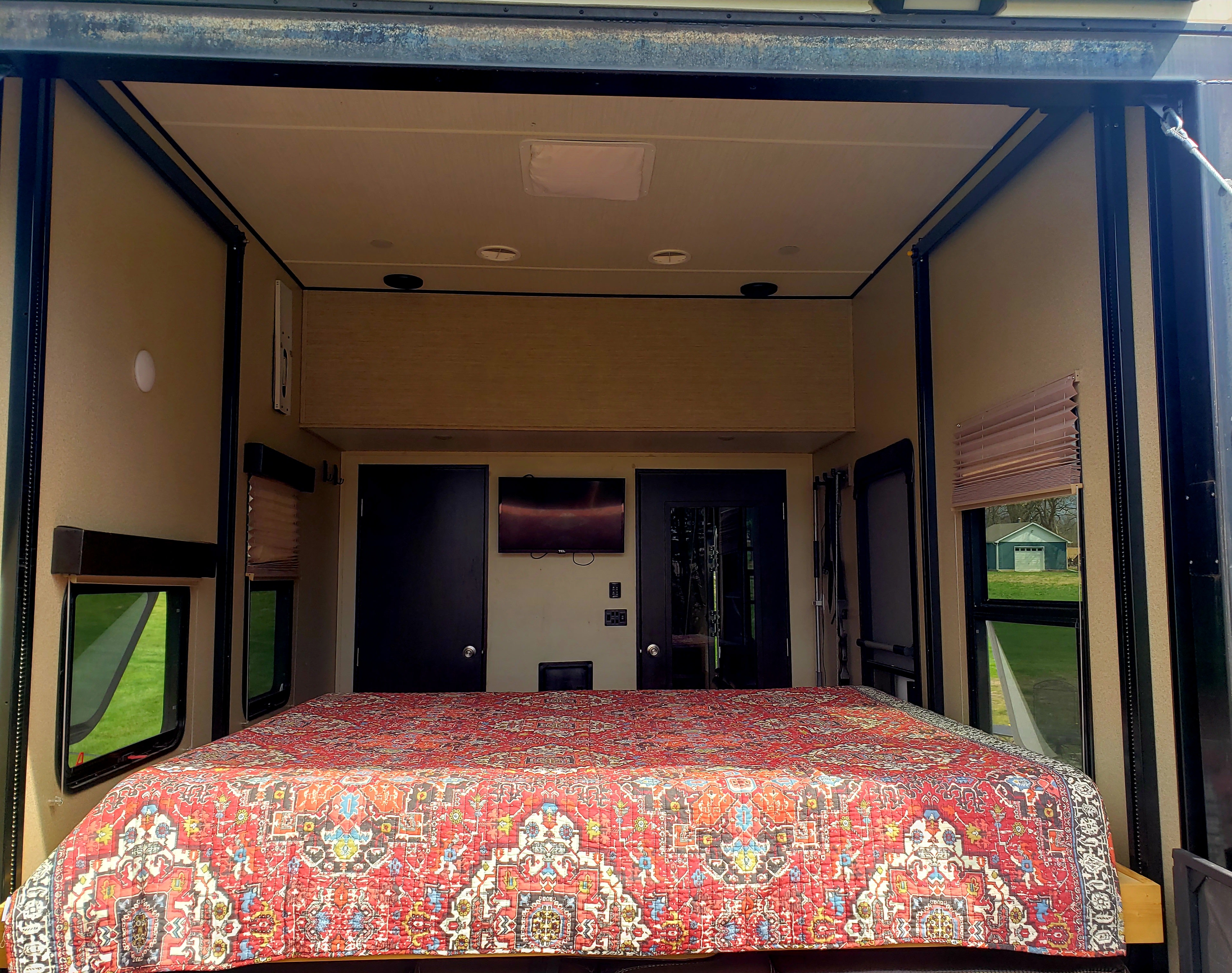 Spacious RV rental bedroom with a large, patterned bed and windows, ideal for comfortable travel.. Grand Design Momentum 2017