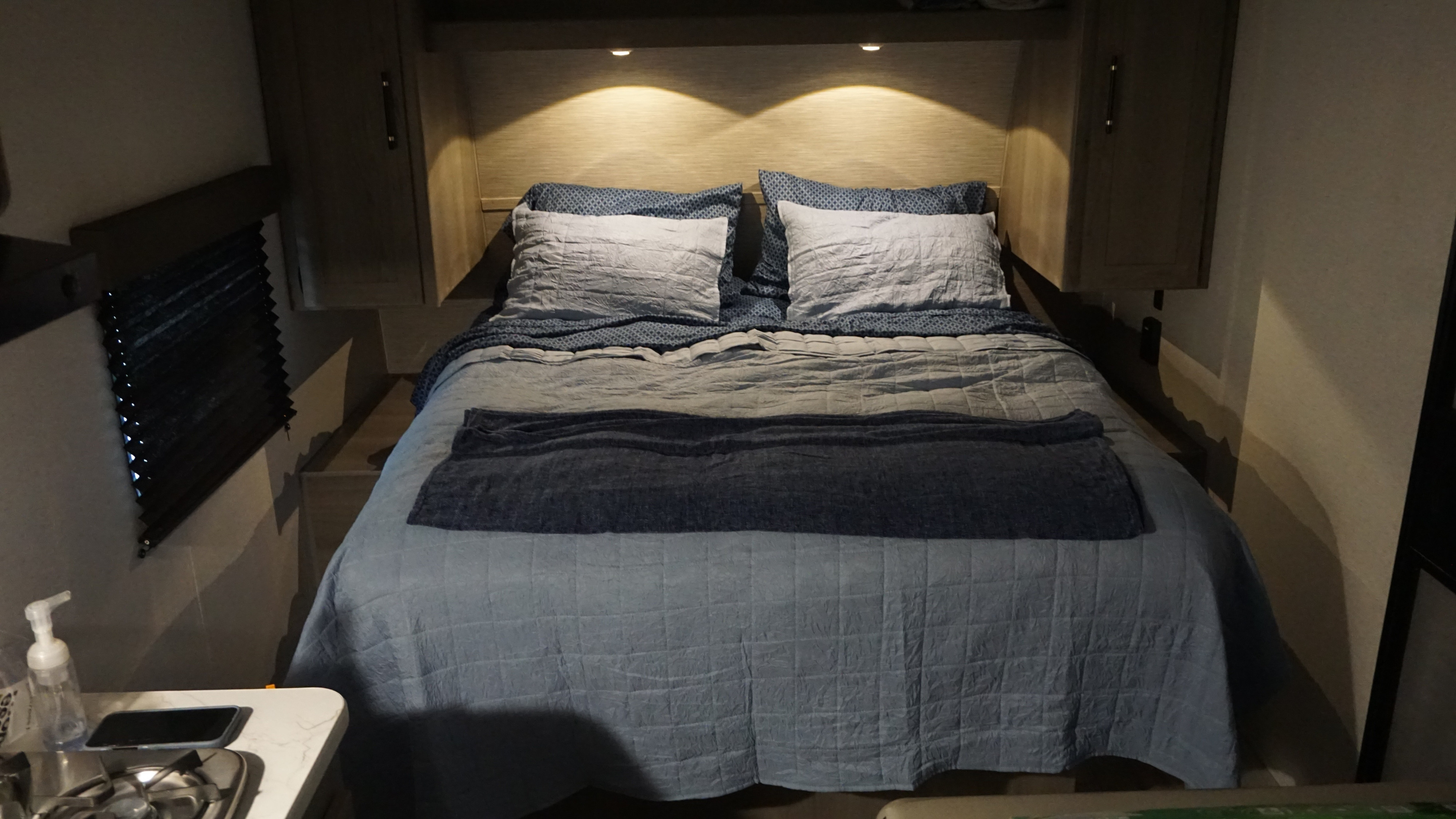 Compact RV rental bed with warm lights, blue bedding, and storage. Ideal for a cozy trip.. Keystone RV Hideout Sport 2025