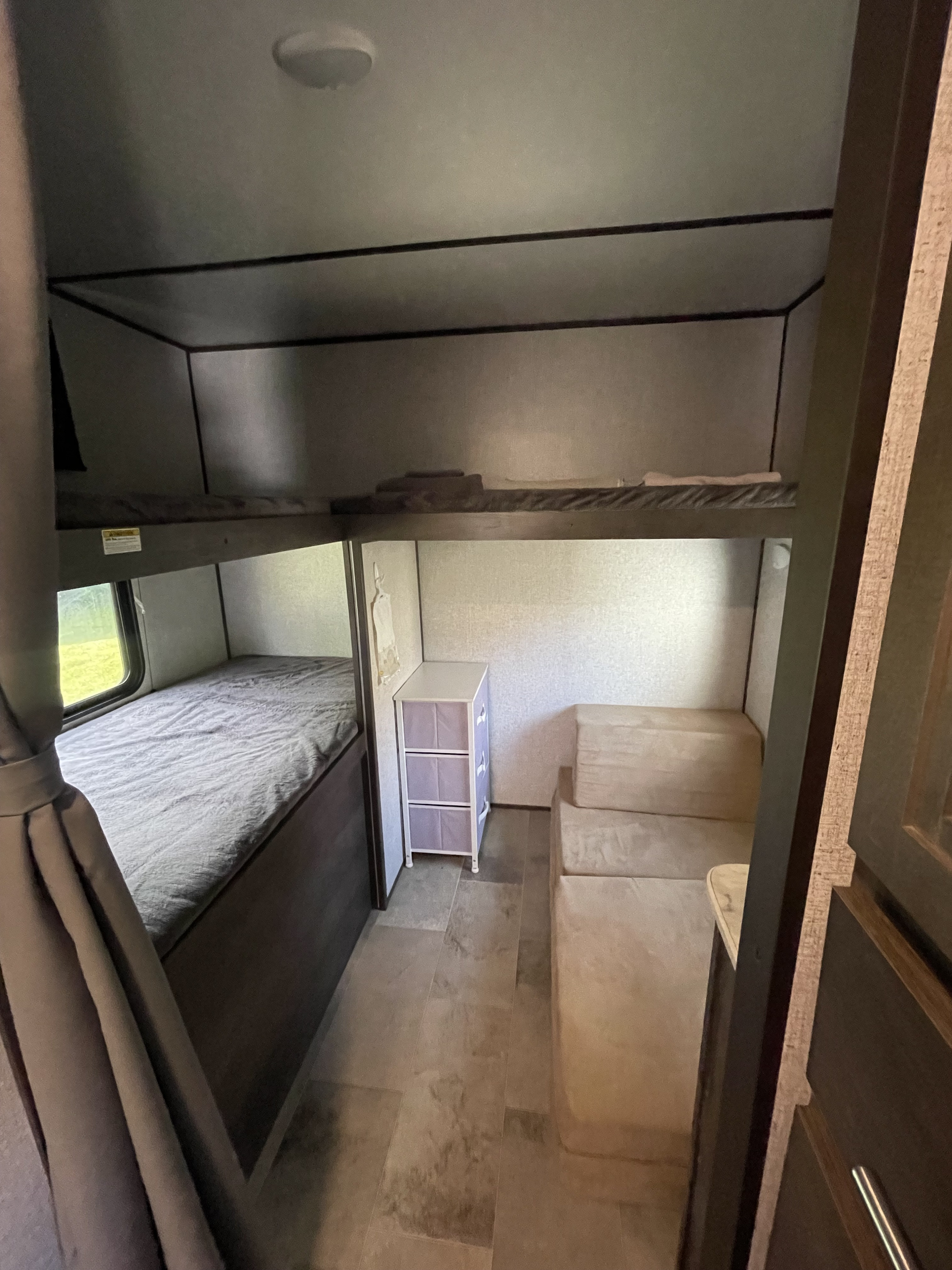 RV rental bunkhouse featuring two beds, a window, a small storage unit with purple drawers, and cozy bench seating on a tiled floor.. Dutchmen Coleman Lantern 2021
