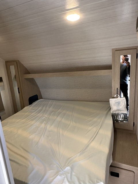 Cozy RV rental bedroom with a bed, overhead shelf, ceiling light, and a moisture absorber near the mirror.. Forest River Wildwood X-Lite 2023