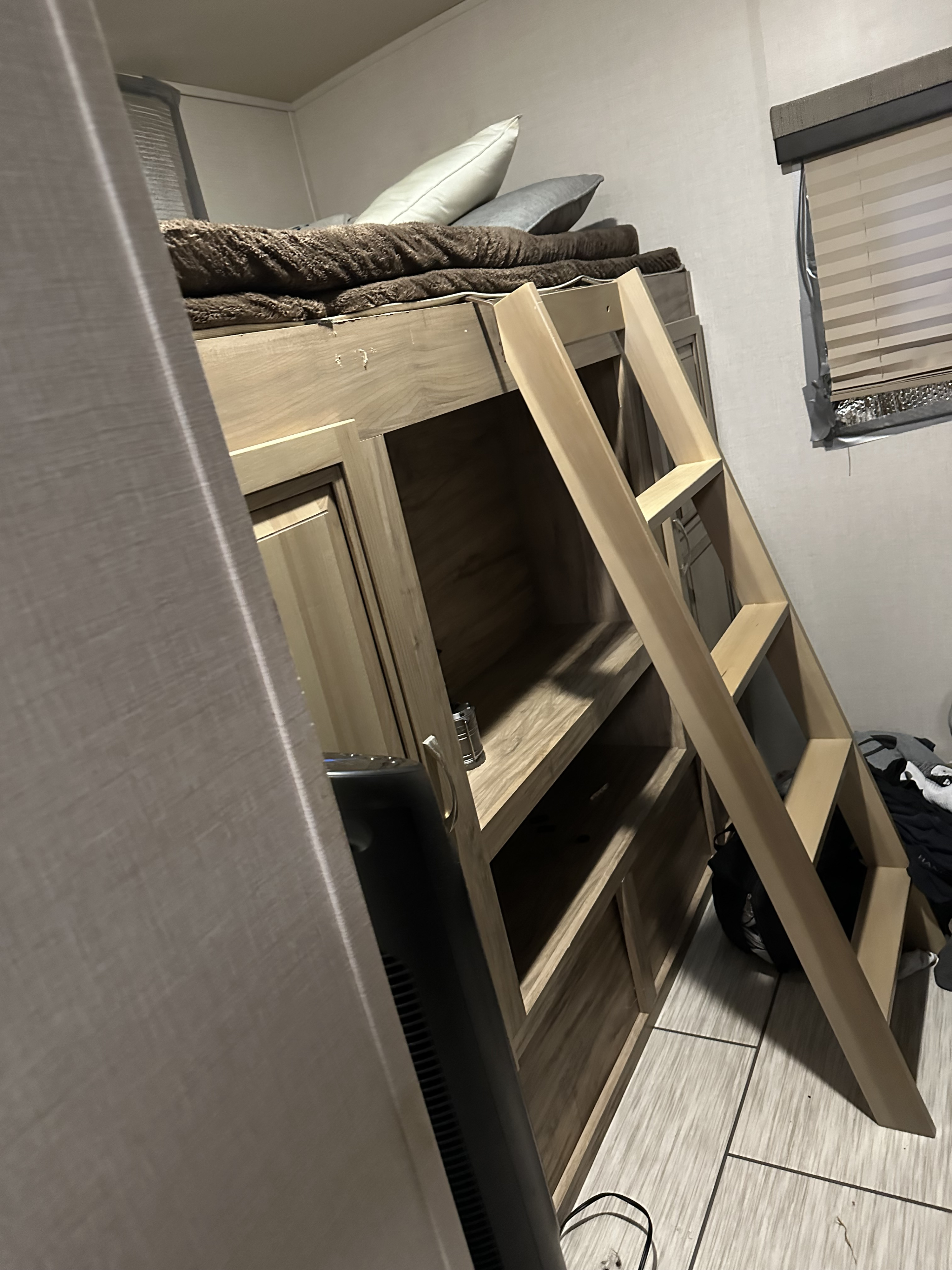 RV rental's functional bunk bed area with soft bedding, a sturdy ladder, and integrated wooden shelves for storage.. Palomino Solaire 2020
