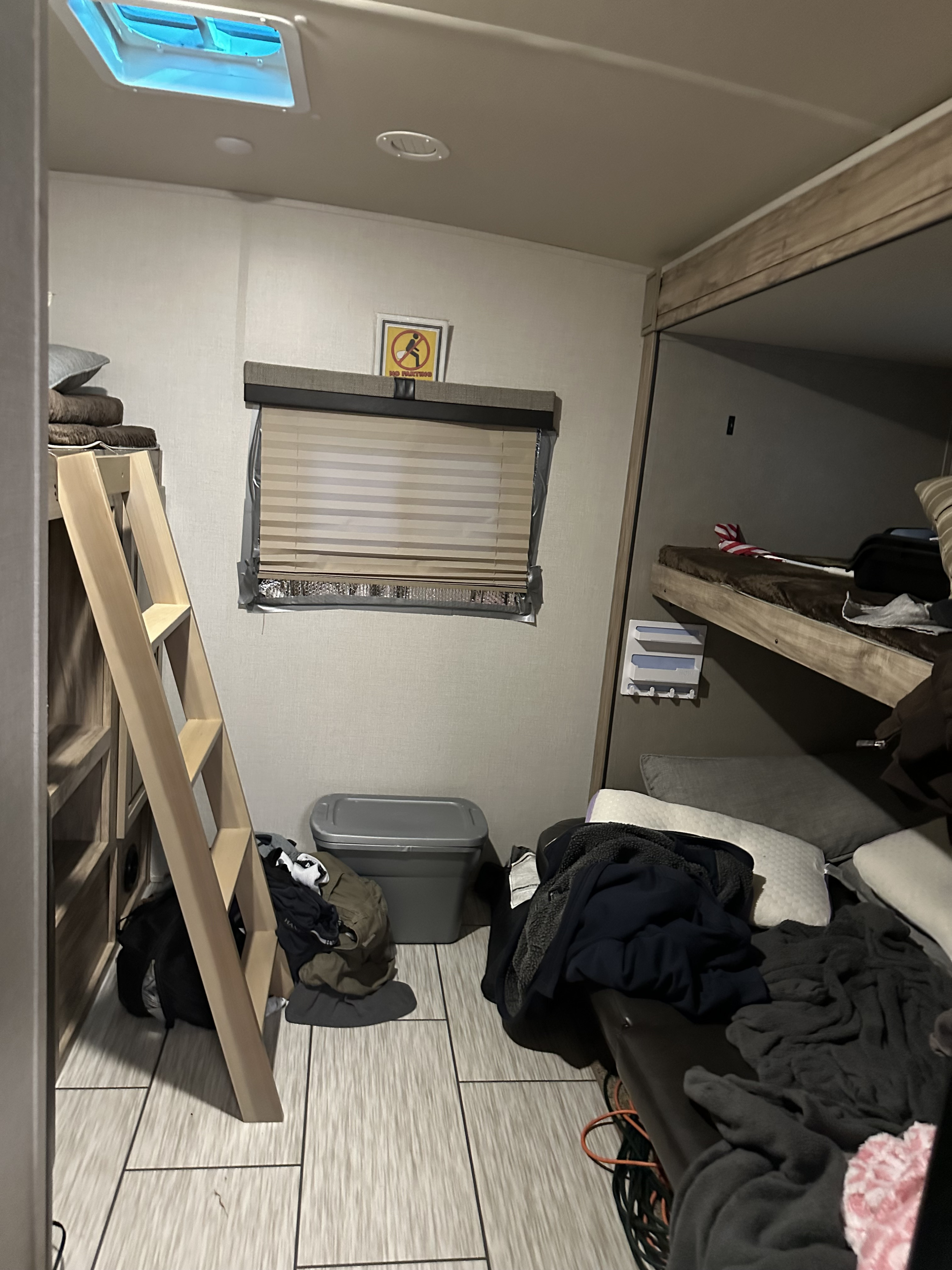 RV rental bunk room: beds, ladder, window with 'No Farting' sign. Cluttered camper interior, storage bin visible.. Palomino Solaire 2020