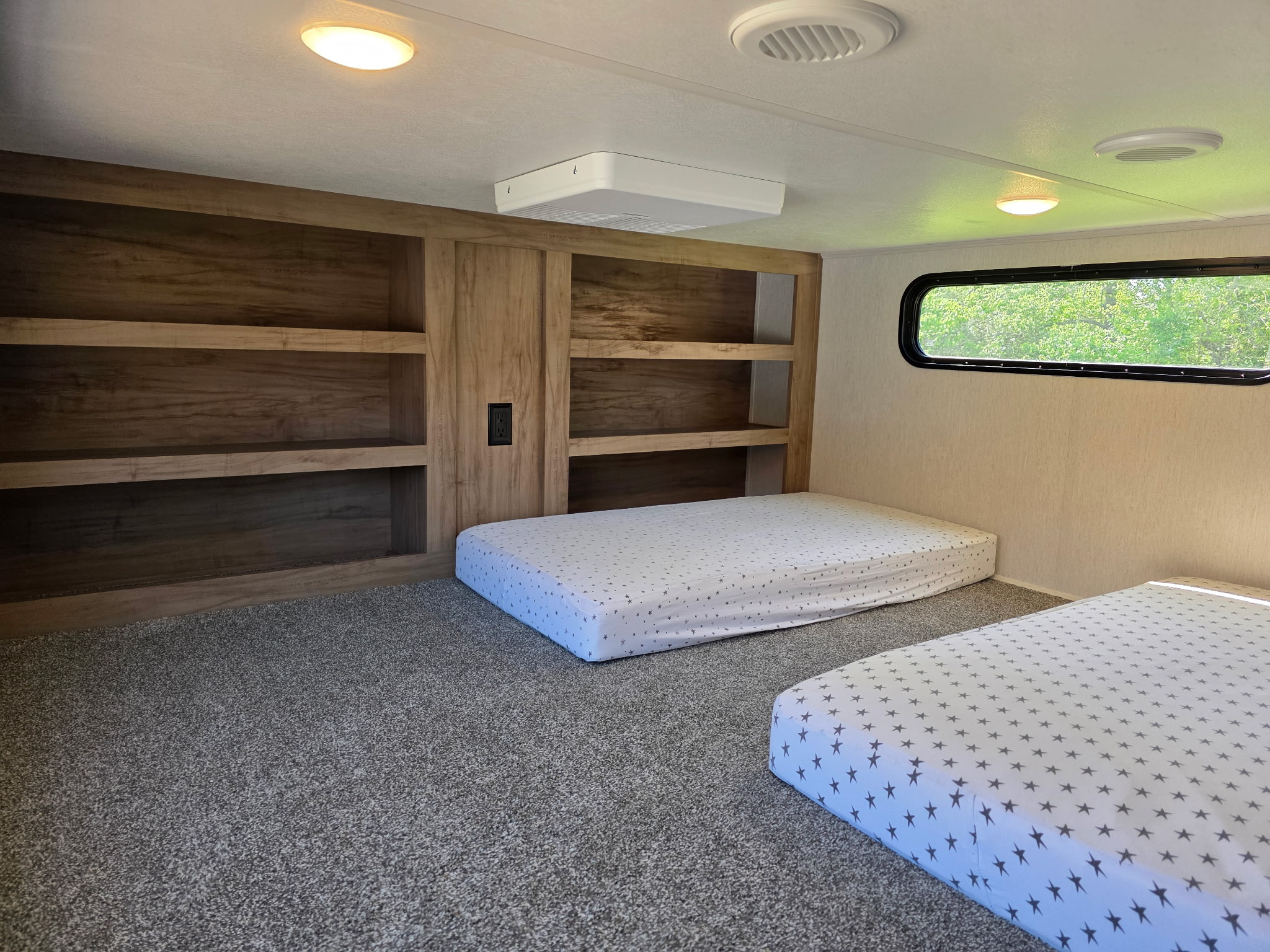 Inside an RV rental: a cozy bunkhouse with two star-patterned mattresses on a carpeted floor, built-in shelves, and a window.. Forest River Sabre 2024