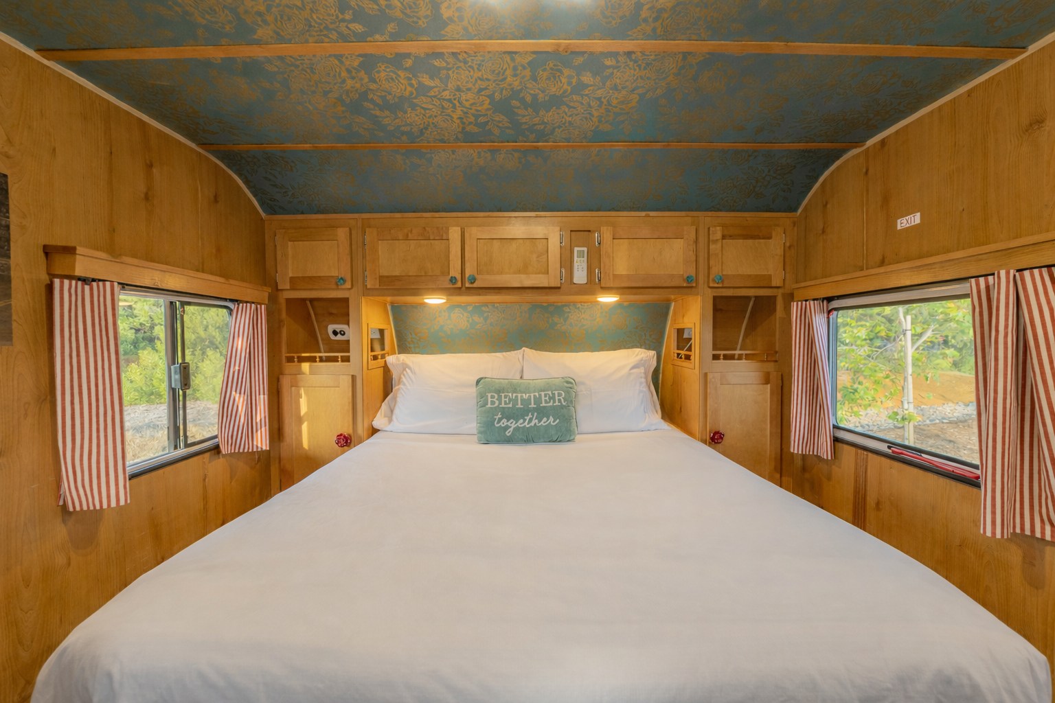 Cozy rv rental bedroom with a spacious bed, wood paneling, unique teal & gold floral ceiling, and windows with striped curtains.. Riverside Travel Trailer Riverside Travel Trailer Trailer 2016
