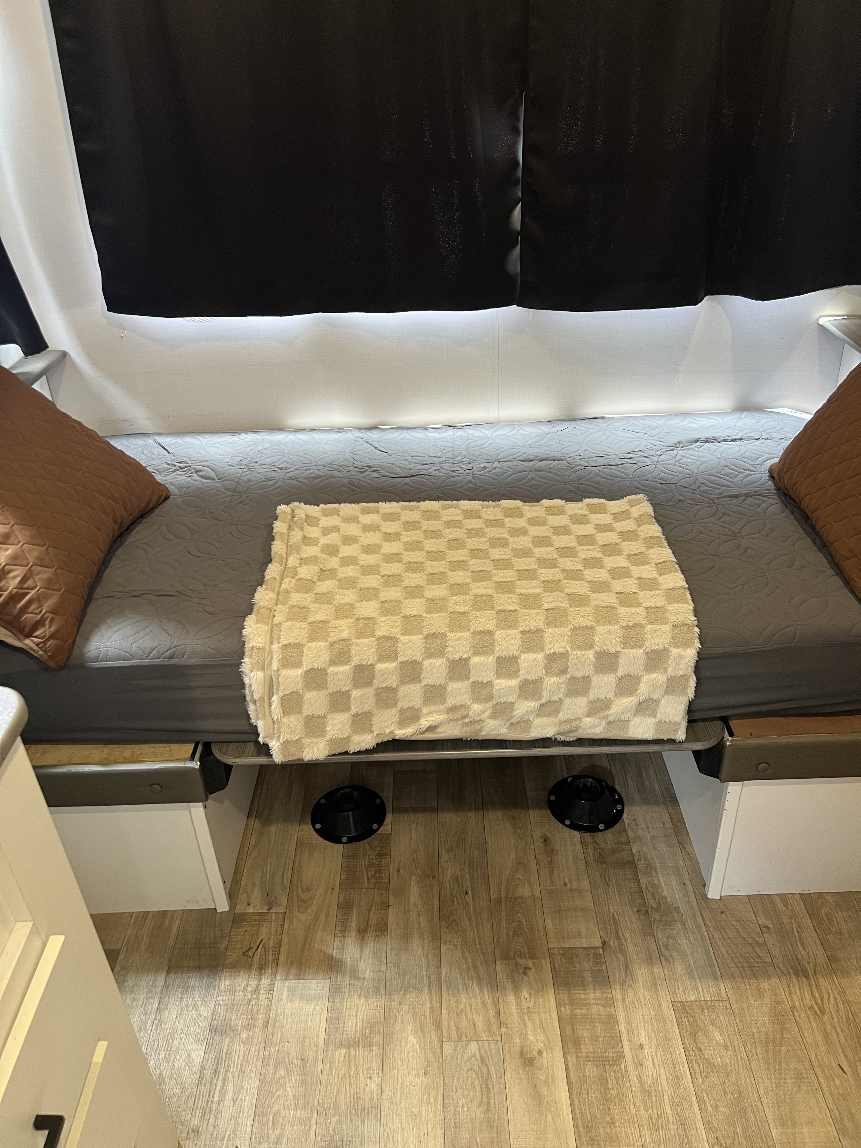 Cozy RV rental interior: A bed with a gray sheet, checkered blanket, brown pillows, and dark pop-up window fabric.. Keystone RV Hideout 2022