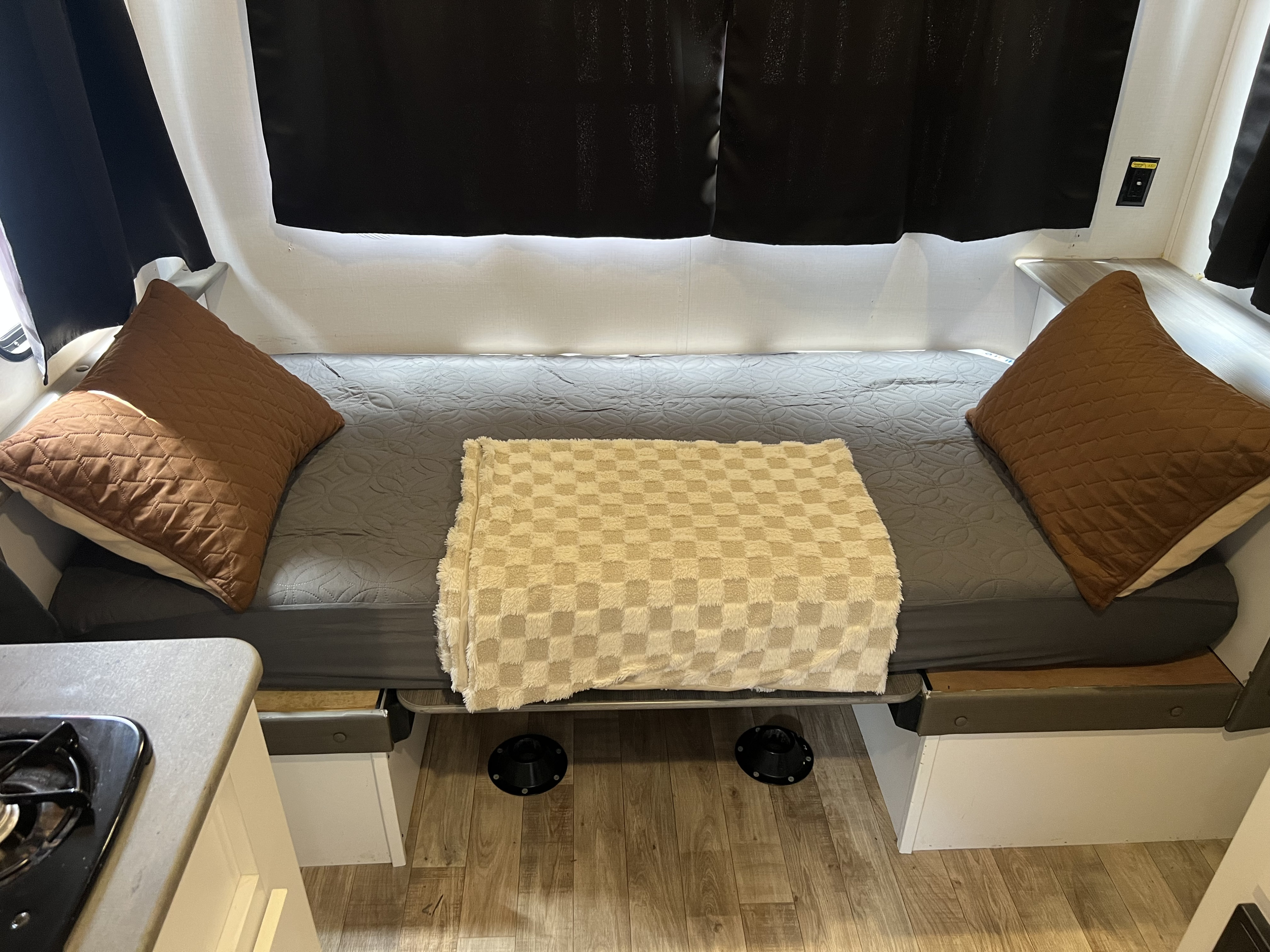 Rv rental interior: A made-up bed with grey mattress, brown pillows, and checkered blanket. Black privacy curtains frame the sleeping area.. Keystone RV Hideout 2022