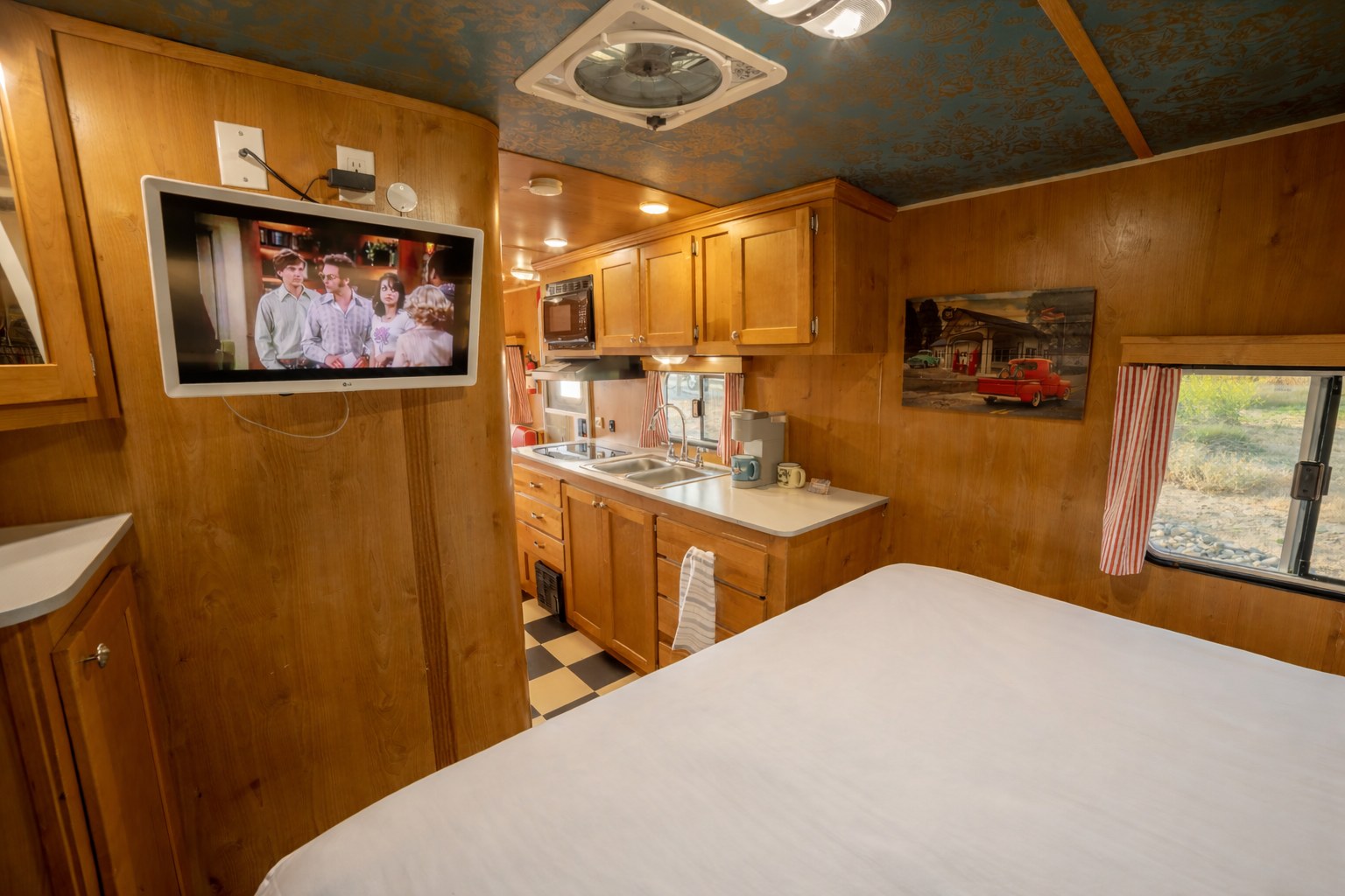 Cozy RV rental interior with a comfortable bed, functional kitchen, wall-mounted TV, and warm wood paneling.. Riverside Travel Trailer Riverside Travel Trailer Trailer 2016