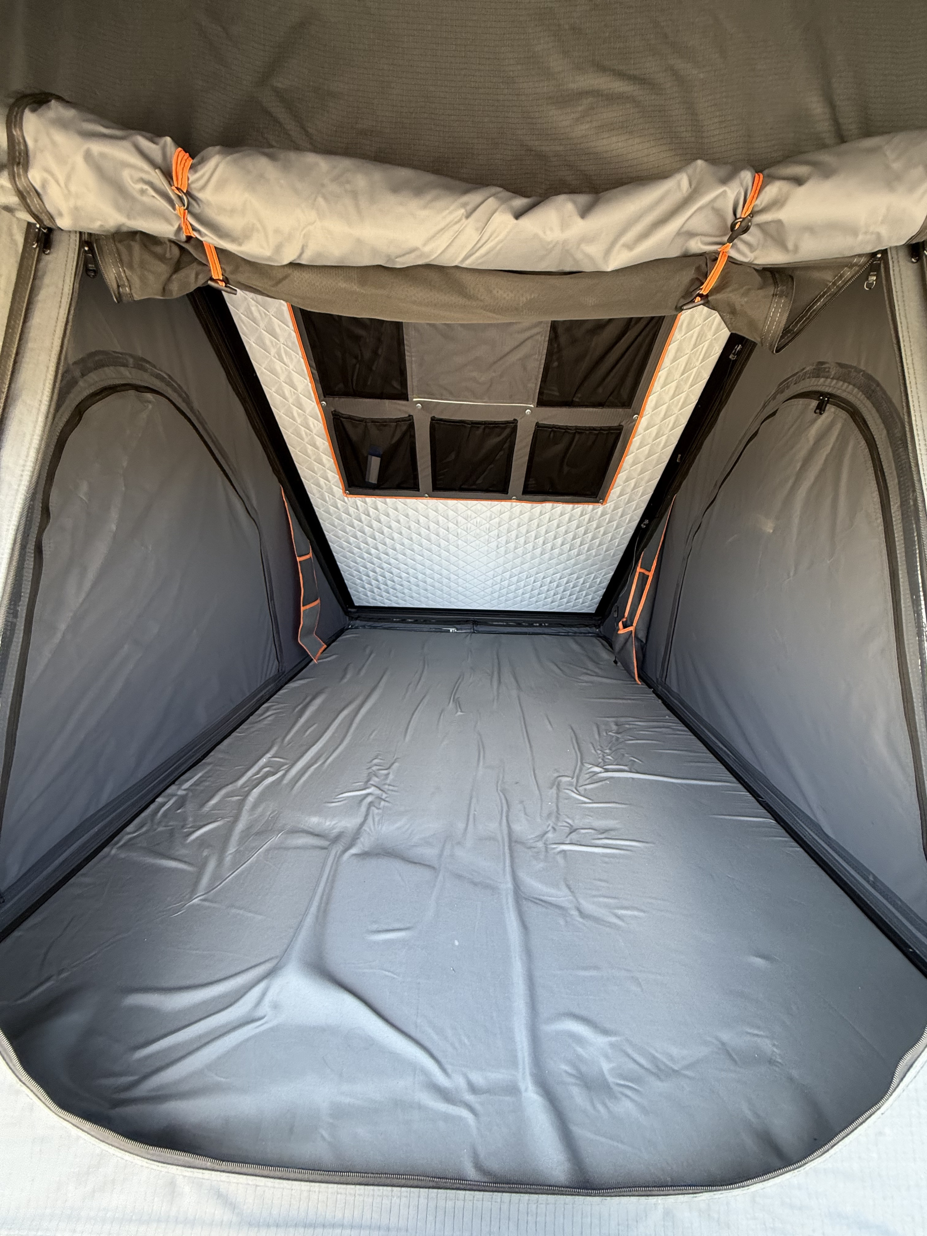 Interior view of an RV rental rooftop tent, featuring a grey sleeping area, quilted ceiling, and storage pockets.. Land Rover LR4 2010