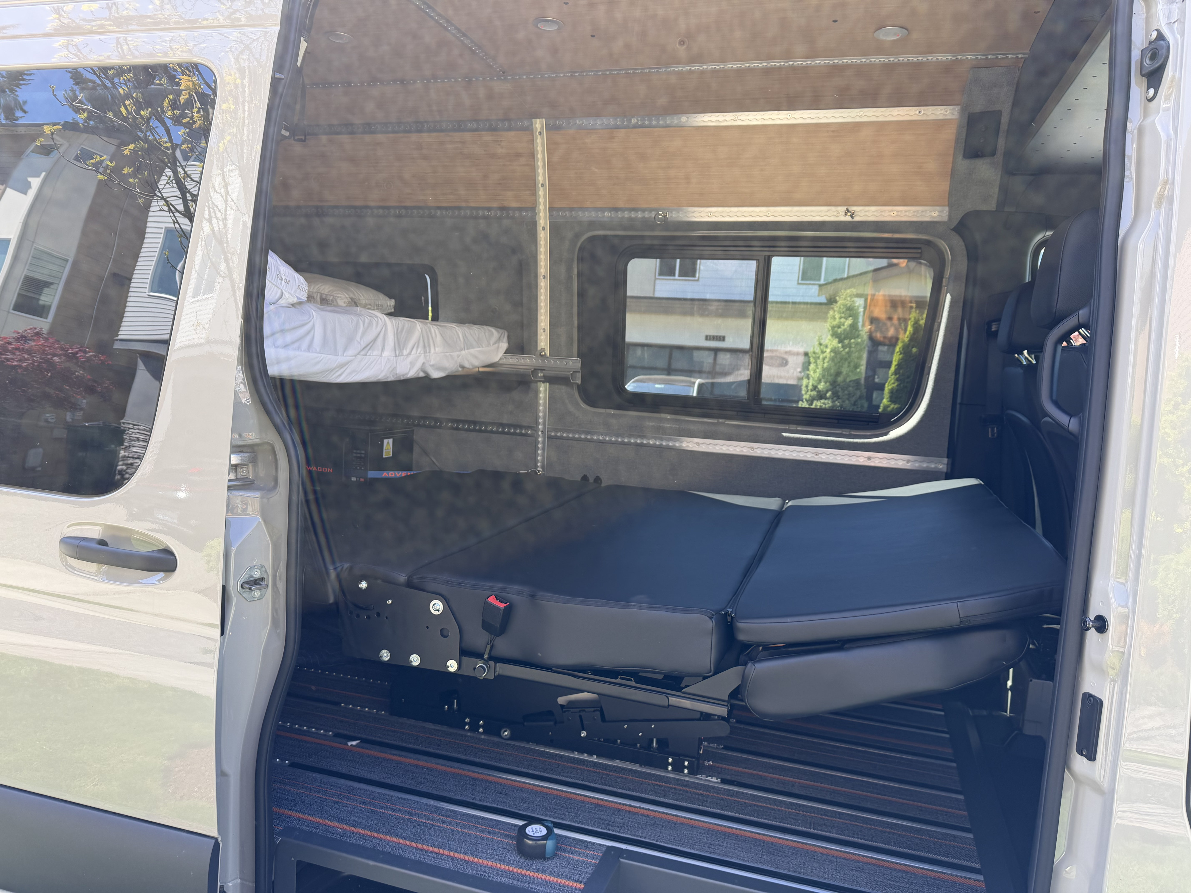 Open side door reveals a well-equipped rv rental interior with a foldable bench/bed, upper bunk, and modular track system for travel.. Mercedes-Benz Sprinter 2025