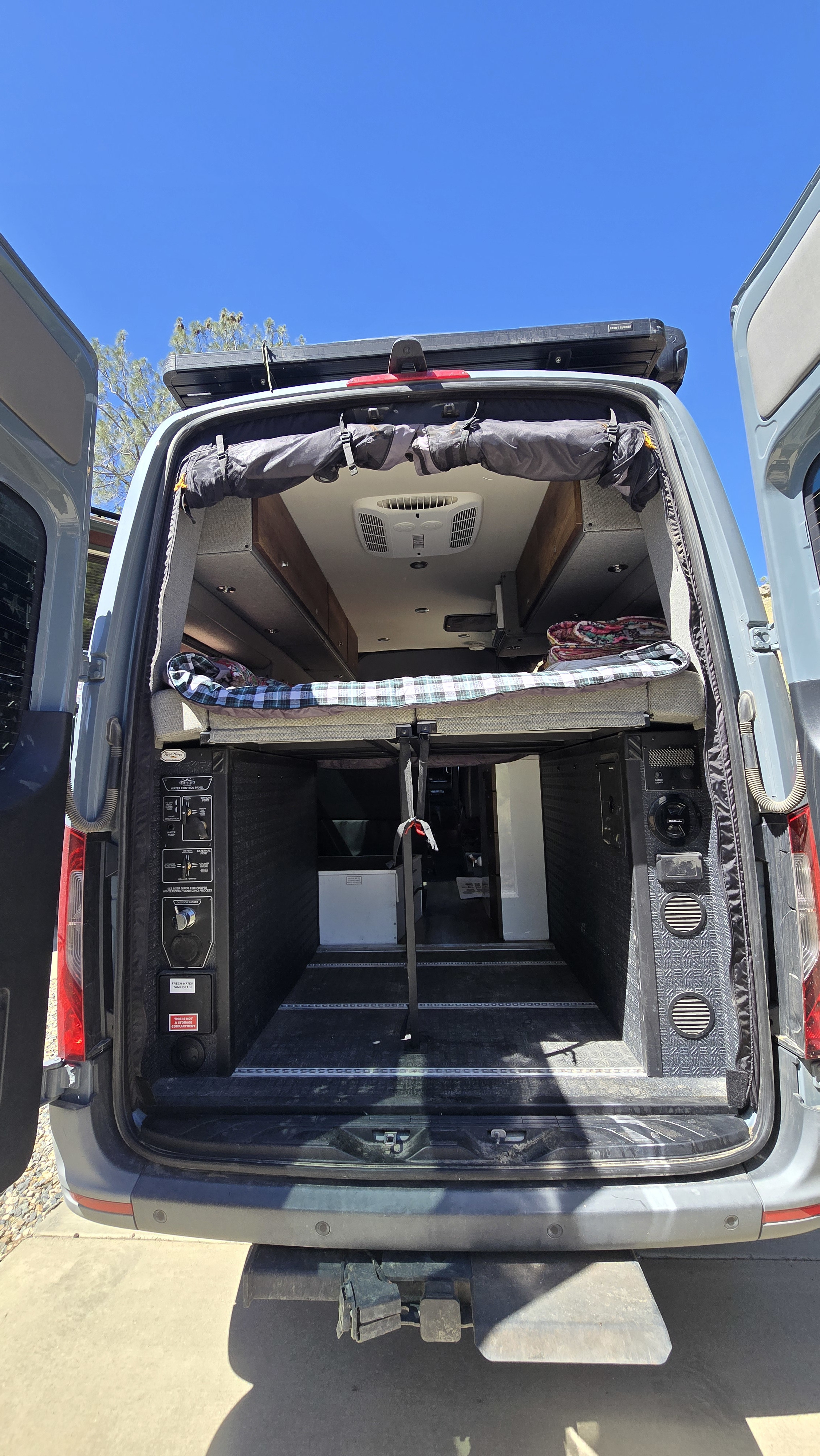Rear of an RV rental camper van shows a raised bed, spacious storage below, and essential utility controls for water and power.. Storyteller Overland Storyteller Overland Class B 2022