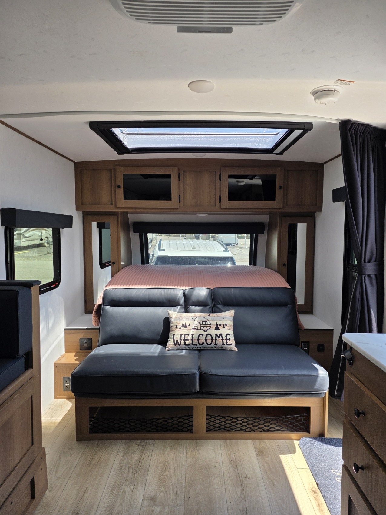 Step inside this rv rental's compact living space: a comfy dark sofa with a 'Welcome' pillow, full bed, wood cabinets, and skylight.. Forest River Coachman Apex Nano 208BHS 2026