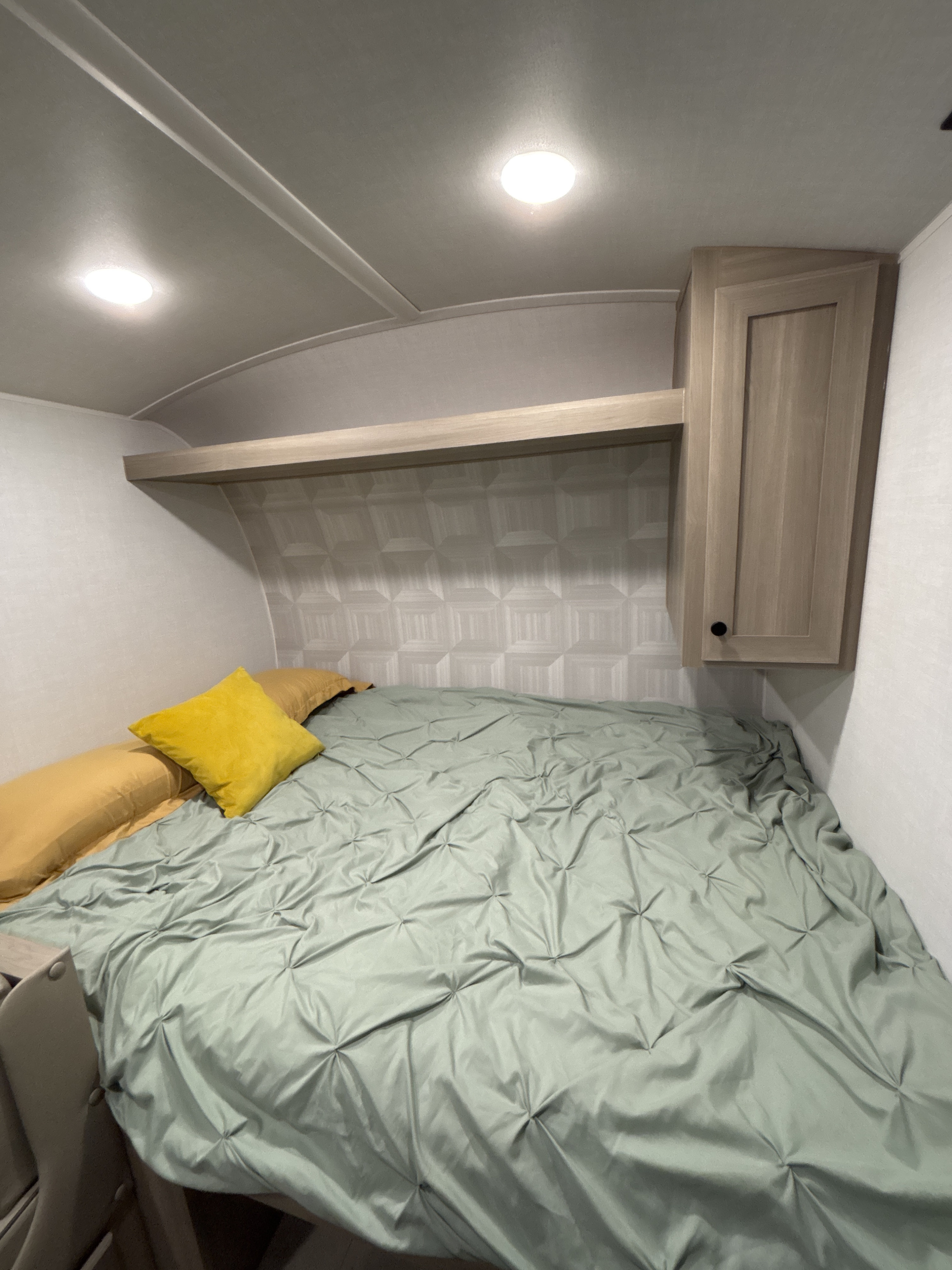 Cozy RV rental bedroom with a comfy bed, overhead storage, bright lighting, and green duvet with yellow pillows.. Forest River Geo Pro 2026