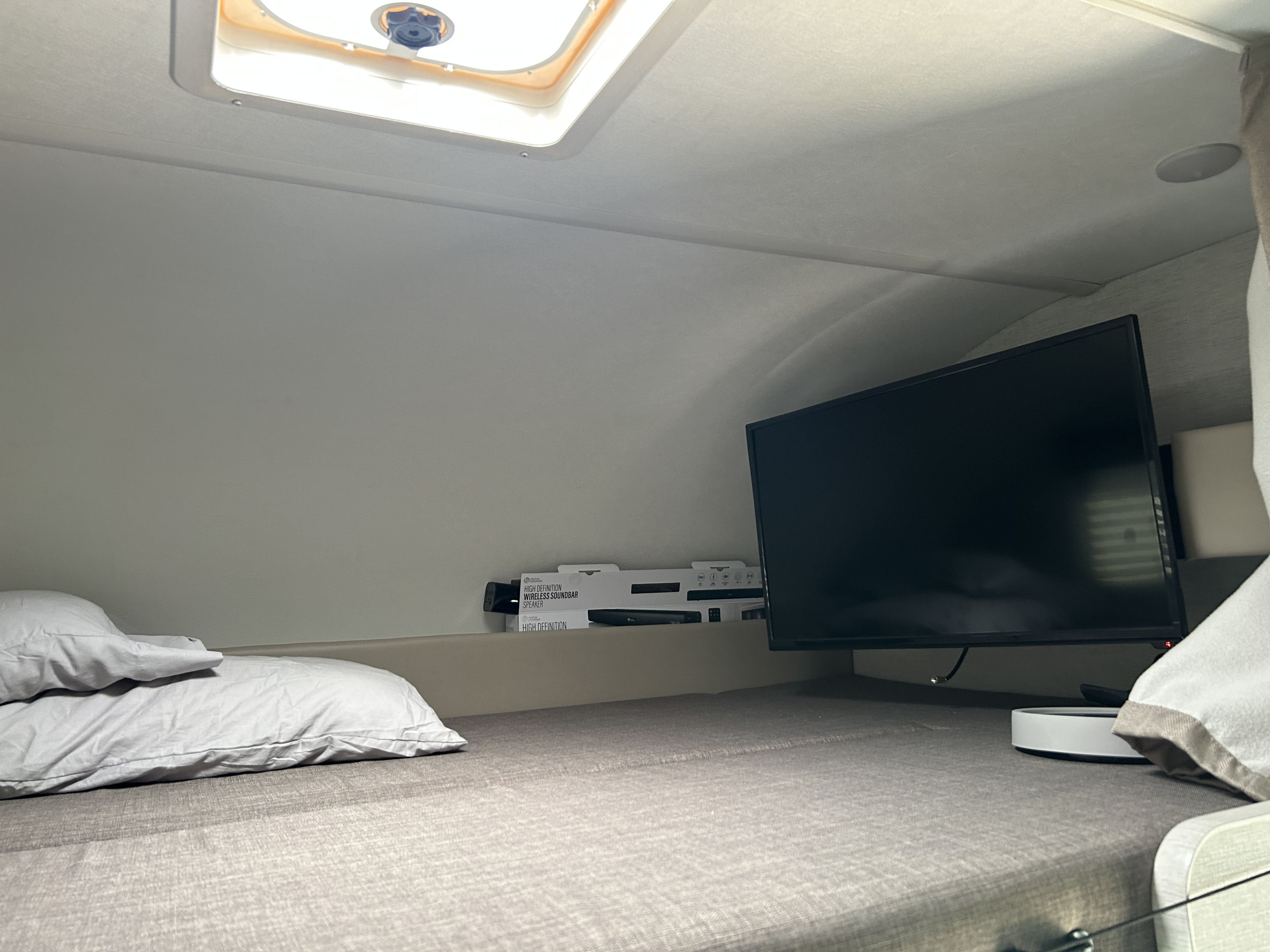 Inside an RV rental: a cozy bed with pillows, a wall-mounted TV, and a ceiling vent.. Thor Chateau 2025