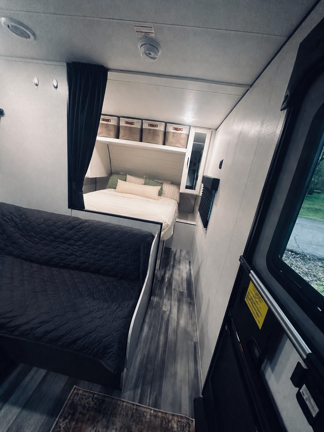 Inside a compact RV rental: a cozy bed, dark futon, storage baskets above, and wood-look flooring. Ready for your adventure.. Jayco Jay Flights 260BH 2026