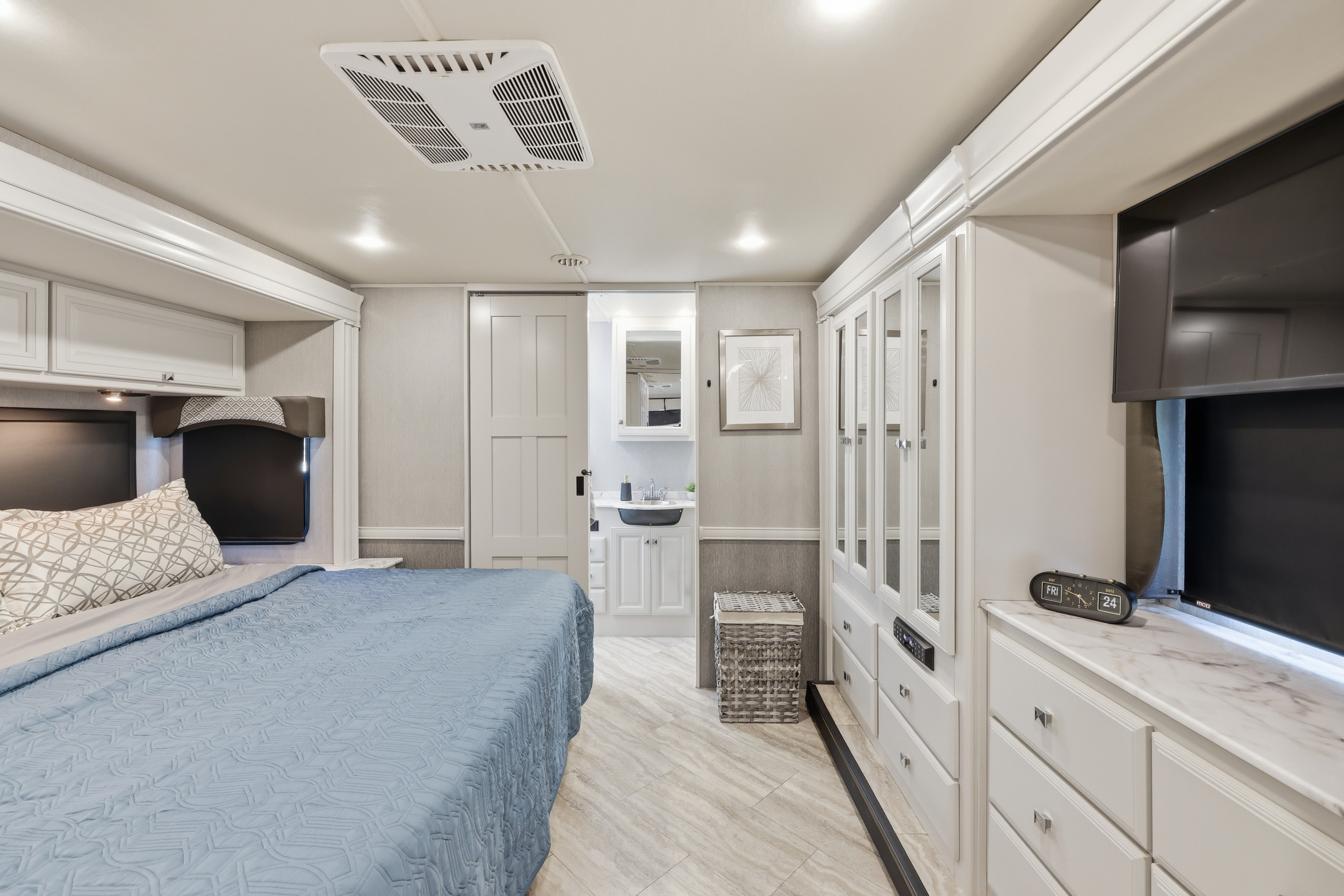 Spacious RV rental bedroom featuring a comfy queen bed, integrated vanity area, ample storage, and a modern TV setup.. Fleetwood Fortis 2021