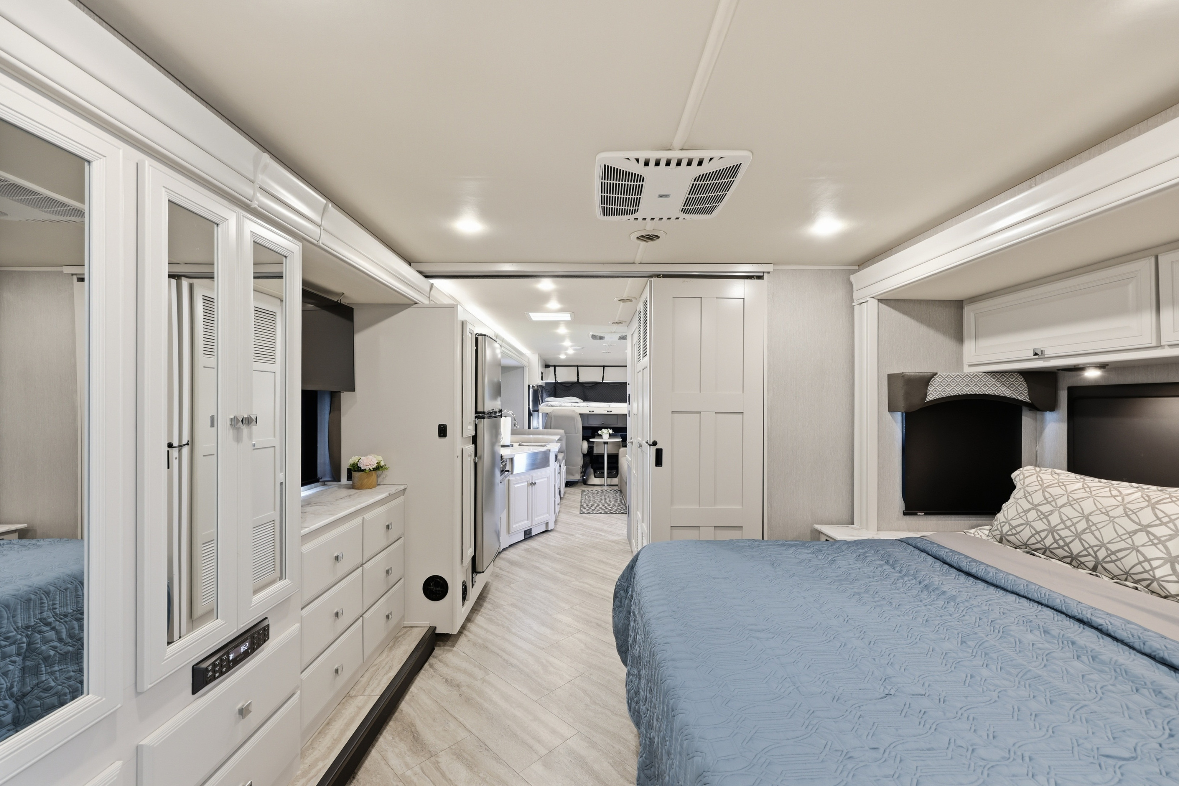 Bright and modern rv rental interior showcasing a bedroom with blue bed, kitchen, and living space.. Fleetwood Fortis 2021