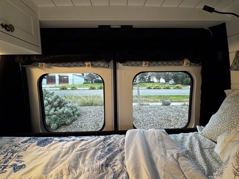 Cozy RV rental interior with bed and windows showing the outside. Perfect for van life adventures.. Dodge Other 2023